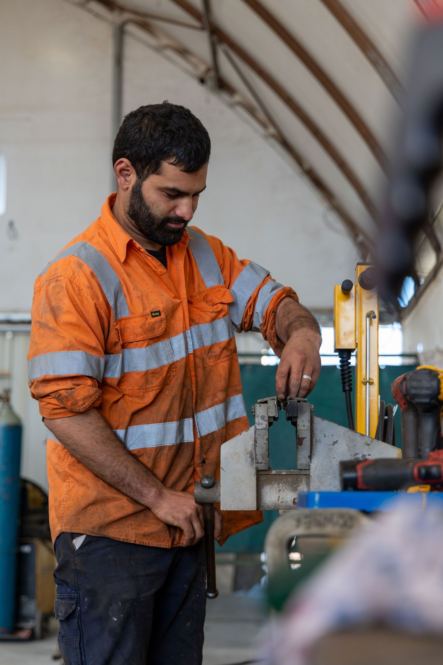 Worker in hi-vis orange safety uniform operating industrial machinery in manufacturing facility.