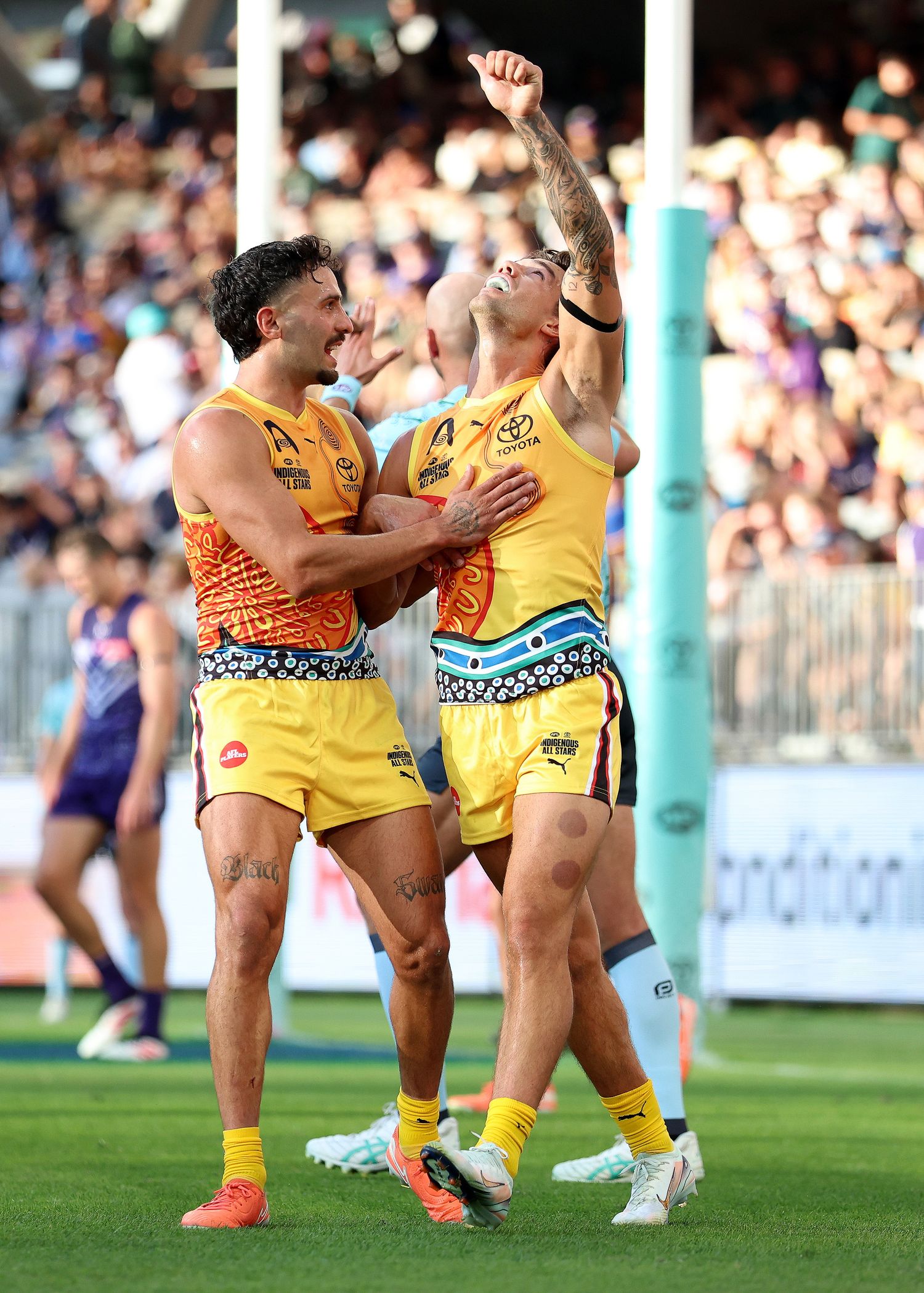Two rugby players in yellow uniforms celebrate together during a match with crowd in background.