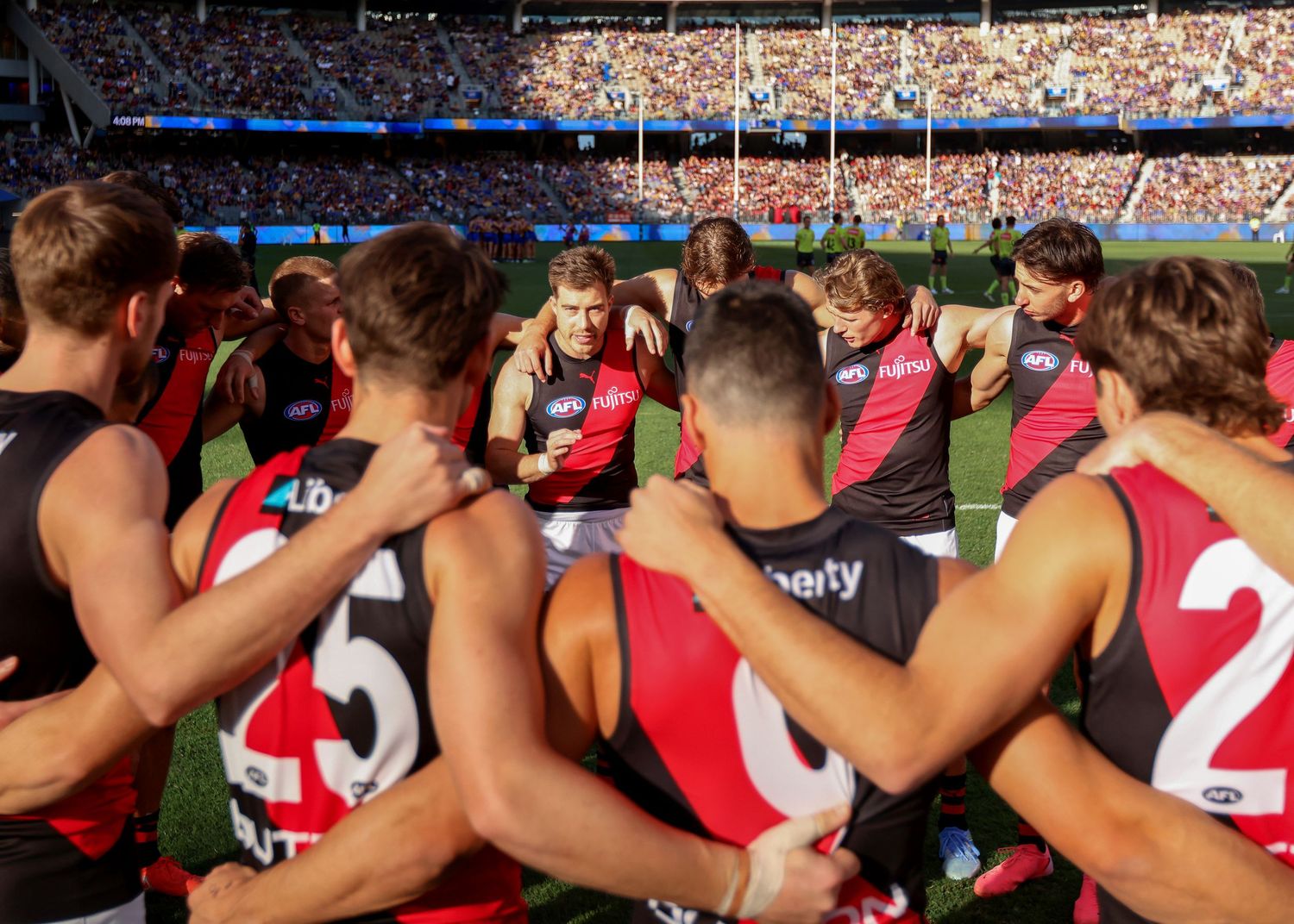 Team huddle of AFL players in red and black uniforms on sports field.