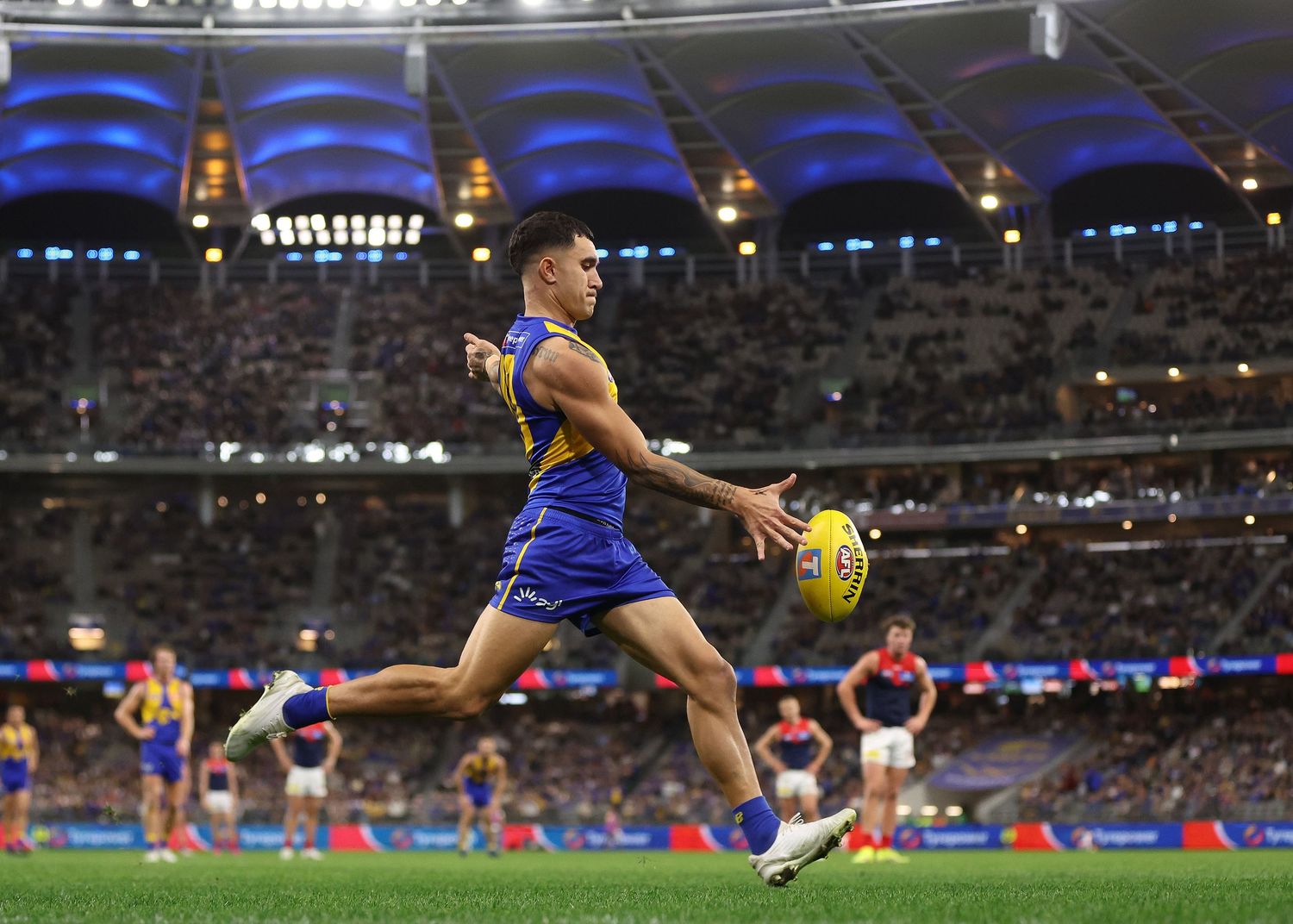 AFL player leaps high to make a spectacular mark attempt in front of a packed stadium.