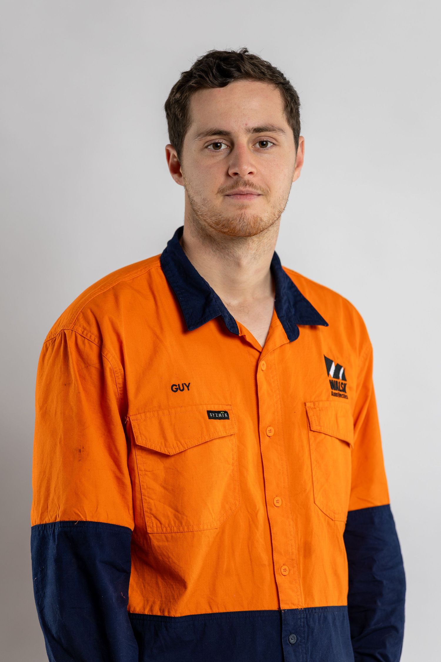Professional studio photo of someone wearing an orange and navy hi-vis work uniform against a light gray background.