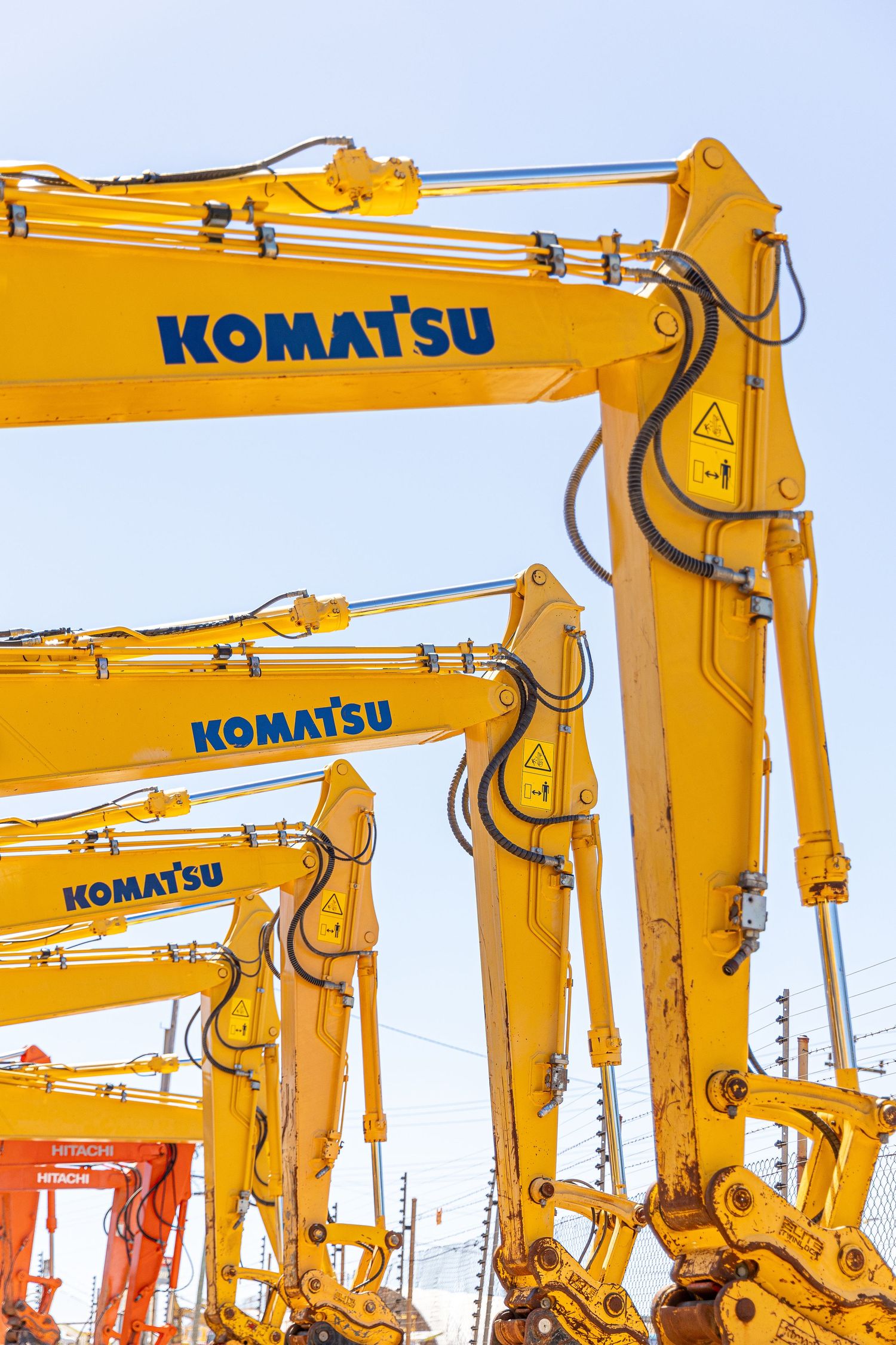 Multiple bright yellow Komatsu hydraulic excavator arms lined up against a light sky with their distinctive branding visible.