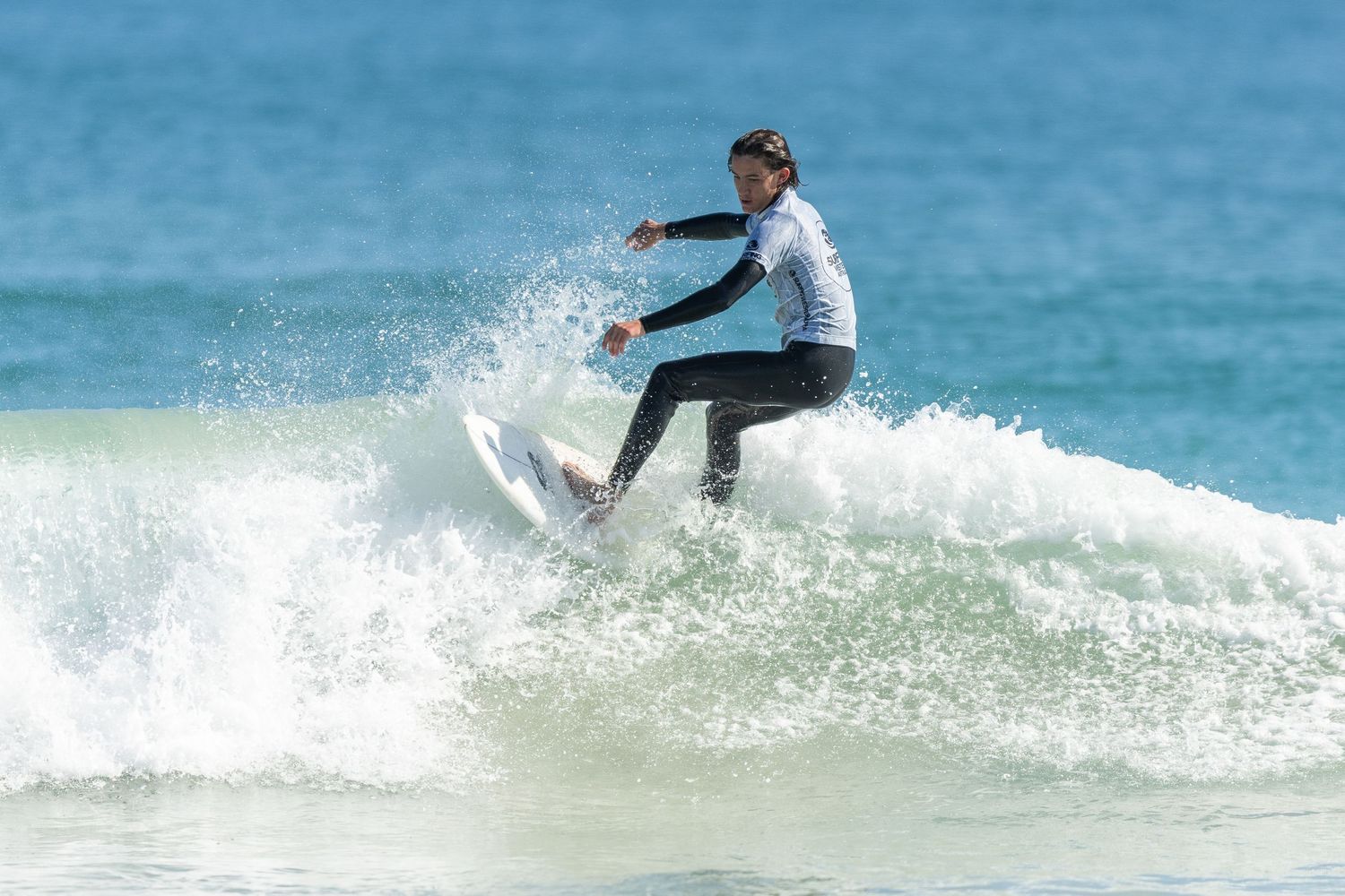 A surfer performs a dynamic turn on a wave while riding a surfboard in blue ocean waters.