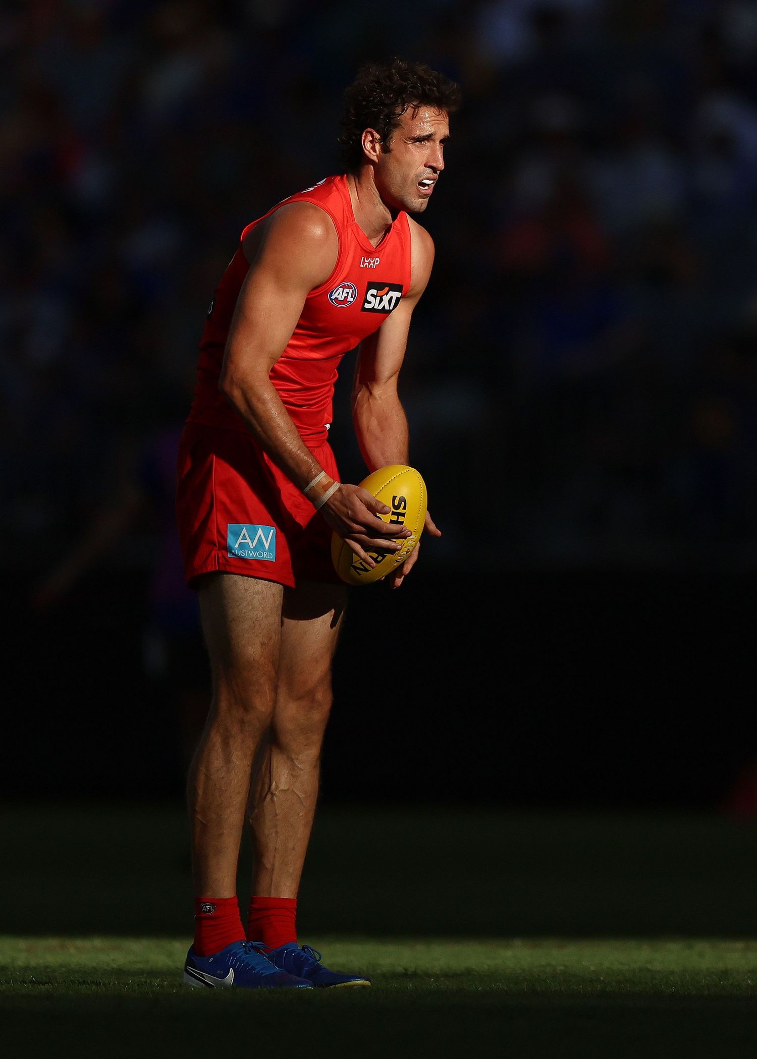 Player in red uniform holds football while standing on field during AFL match.