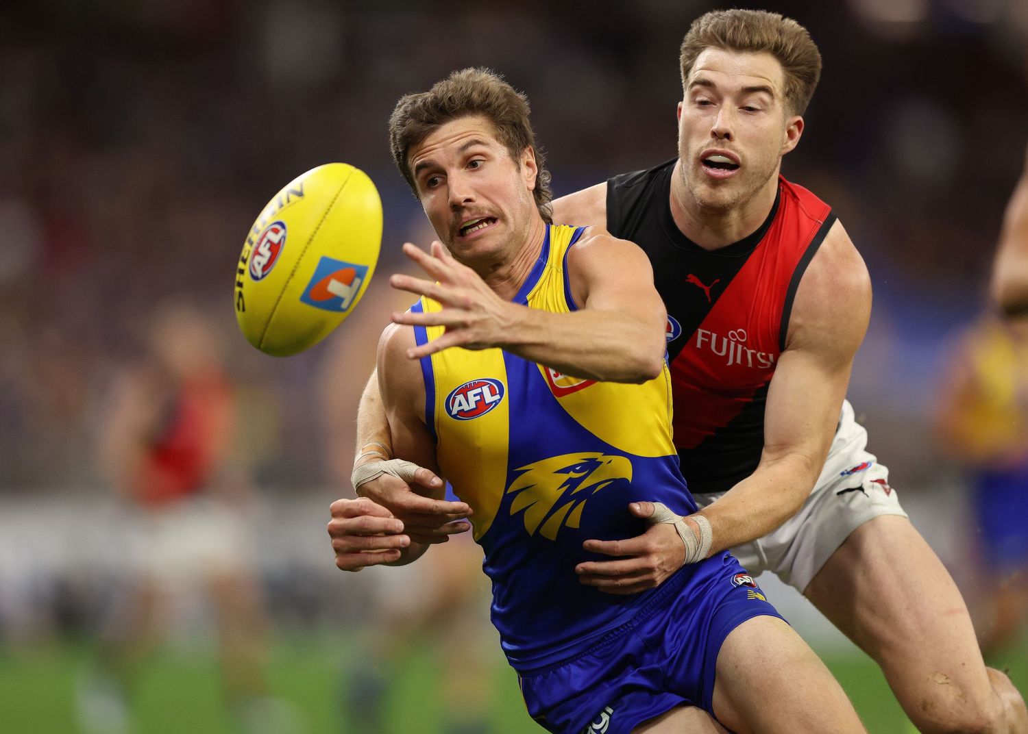 Two AFL players compete for possession of the ball during intense match action.