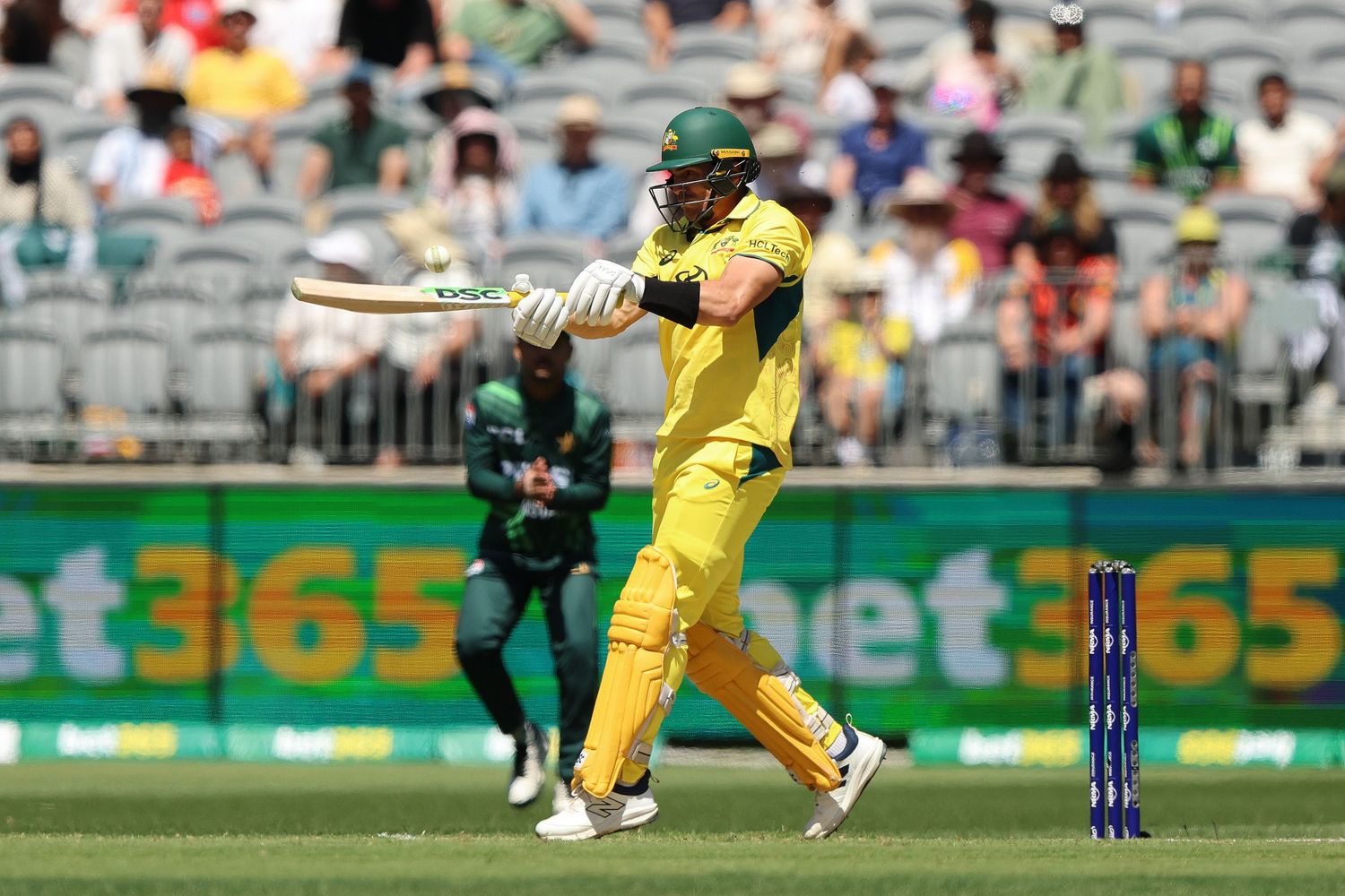 Cricket player in yellow uniform swinging bat during match.