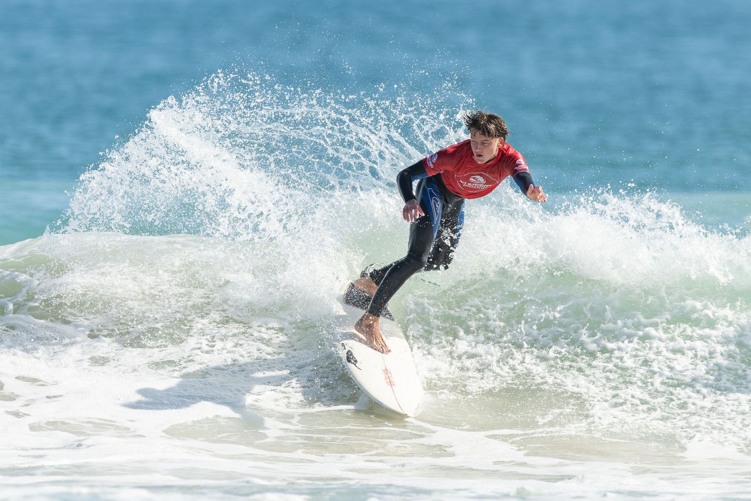 A surfer riding a wave performs a sharp turn, spraying water behind them on a bright turquoise ocean.