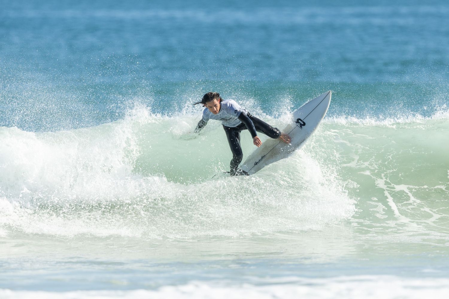 A surfer performs an impressive aerial maneuver on a turquoise wave during a surfing competition.