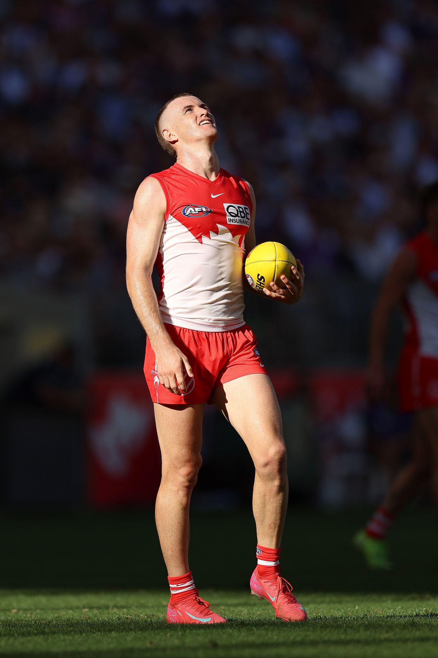Player in red and white uniform stands with football on sunny field during match.