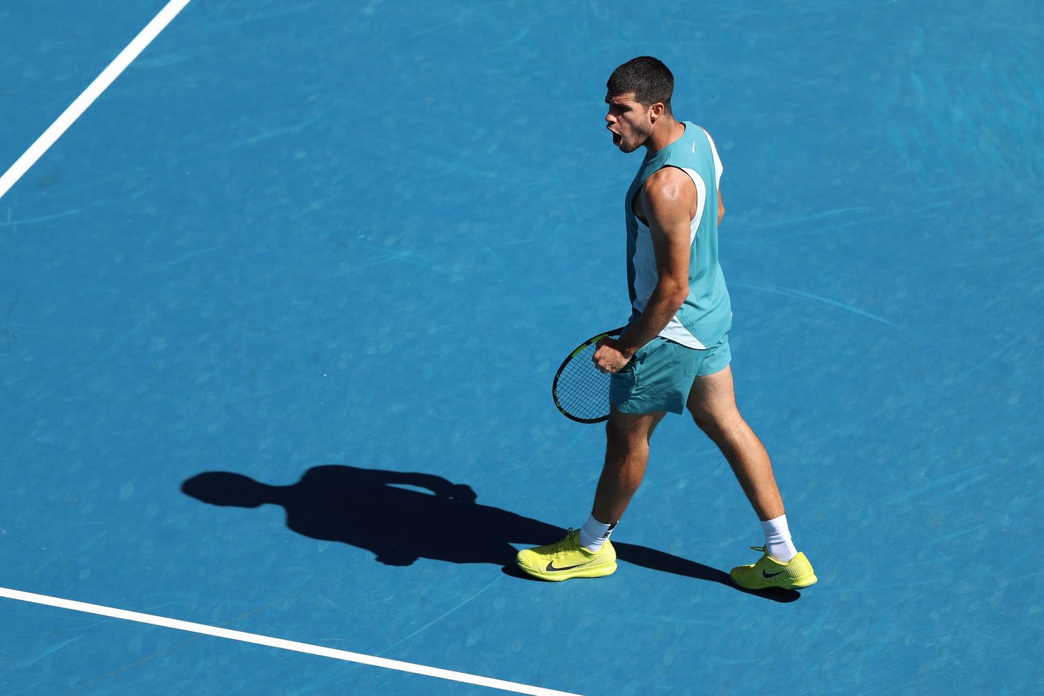 Tennis player in light blue outfit casts shadow while playing on blue court.