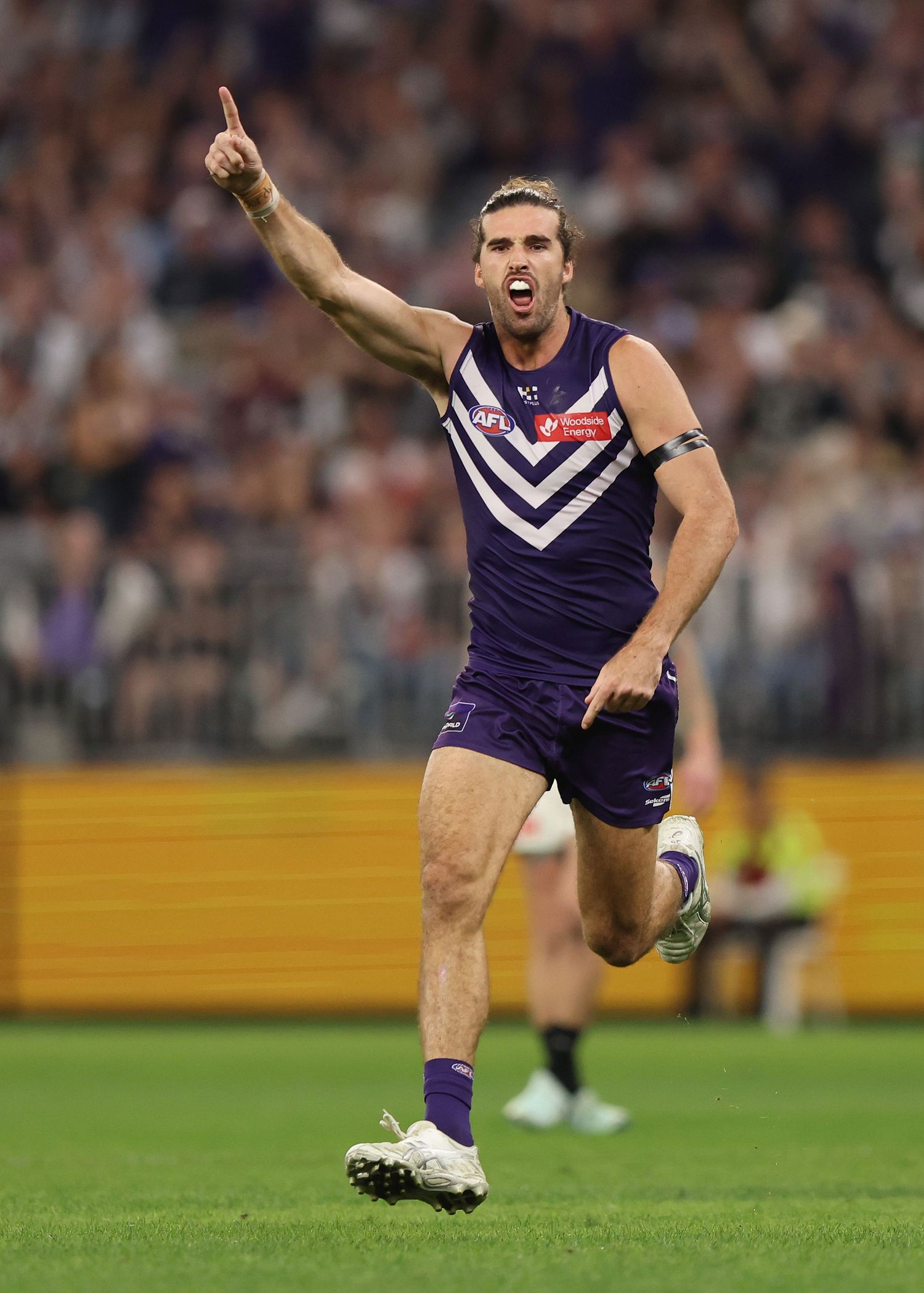 Player in purple uniform celebrates after scoring during AFL match.