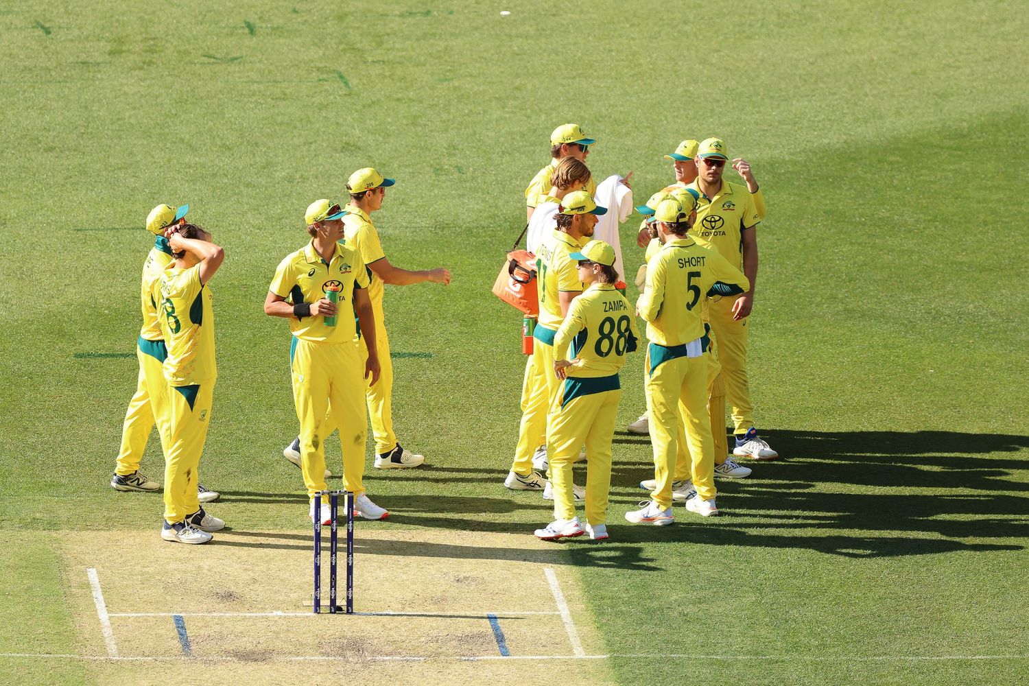 Cricket team in yellow uniforms gathered on field during match.