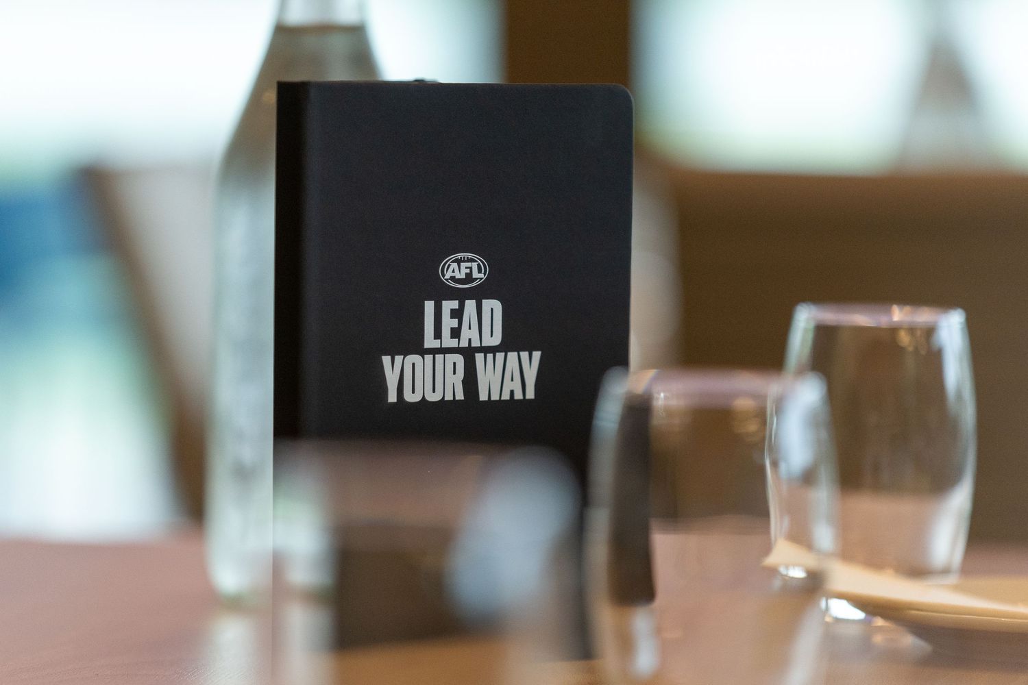 A black notebook with 'Lead Your Way' text sits on a restaurant table next to water glasses.