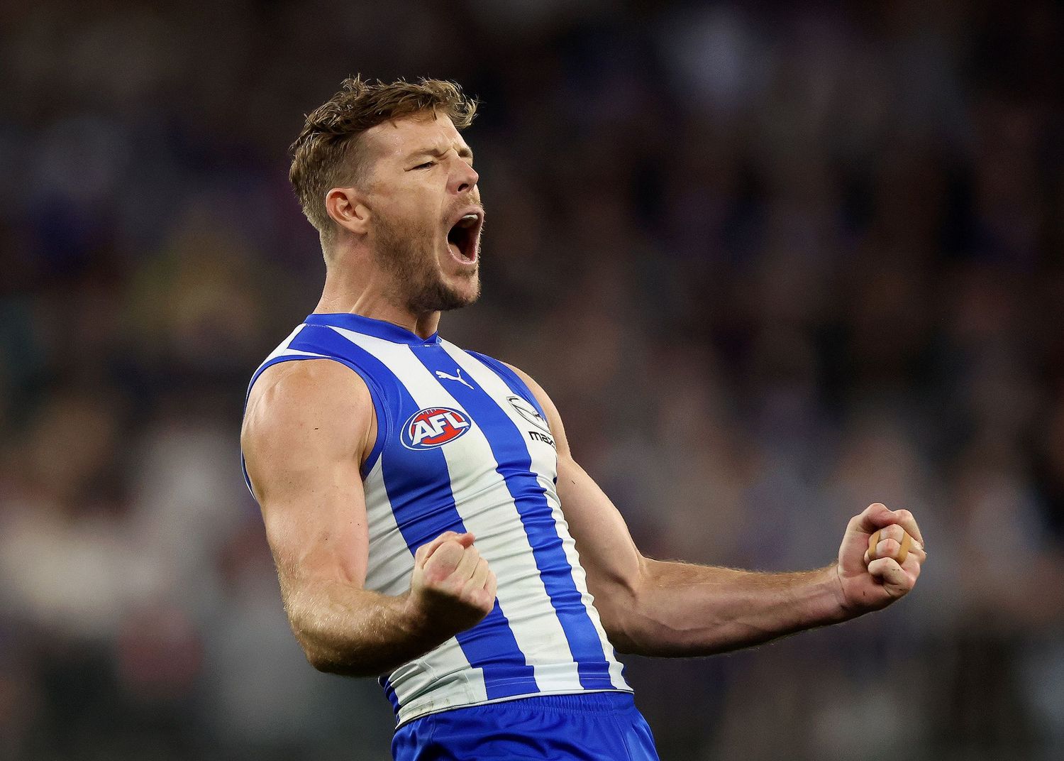 AFL player celebrates passionately with fist pump in North Melbourne Kangaroos blue and white striped jersey.