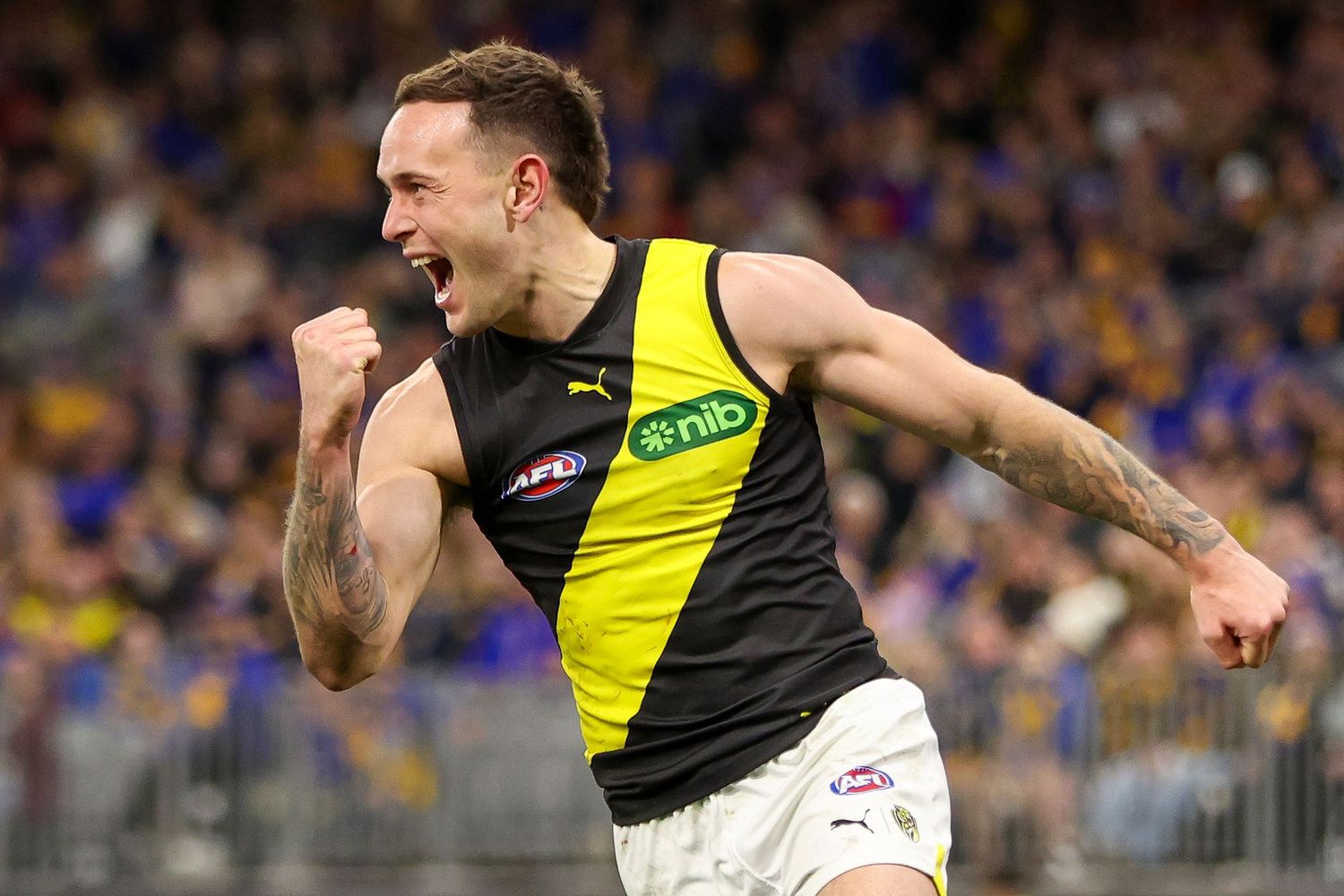AFL player in Richmond Tigers yellow and black uniform celebrates with emotion during game at crowded stadium.