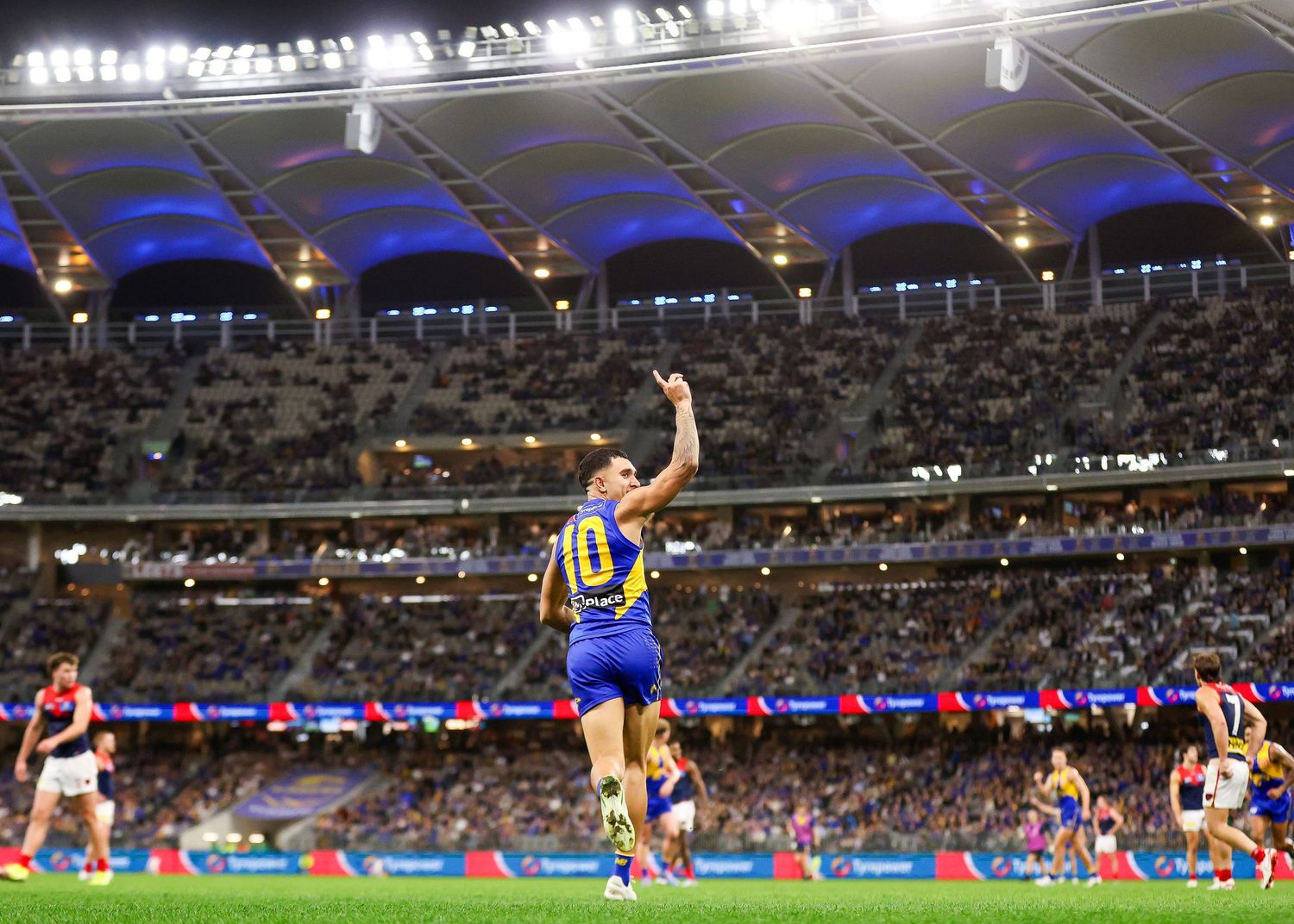 A football player leaps high to catch a ball during a night match in a large illuminated stadium.
