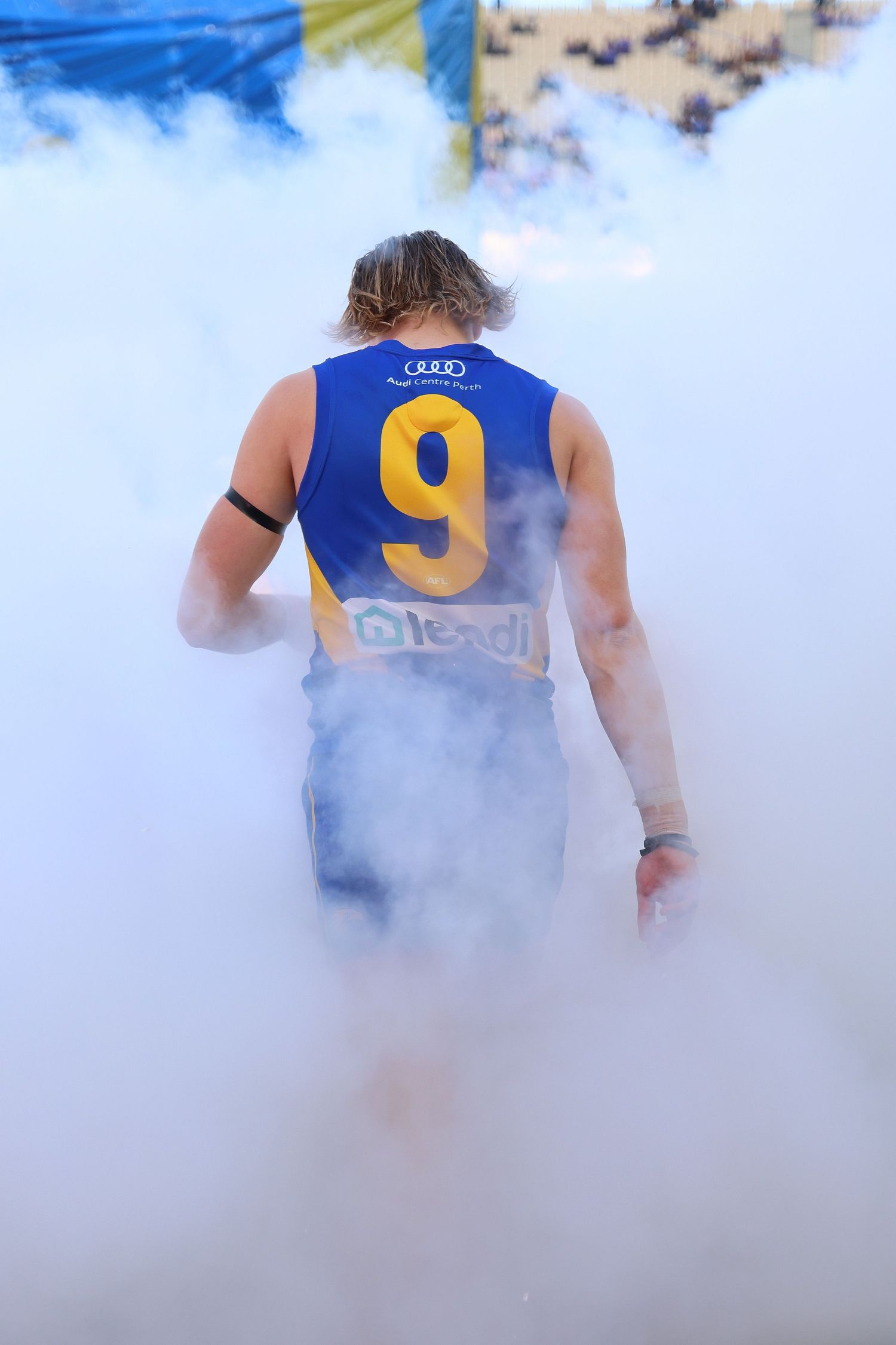 AFL player in blue jersey number 9 walks through smoke during game entrance.