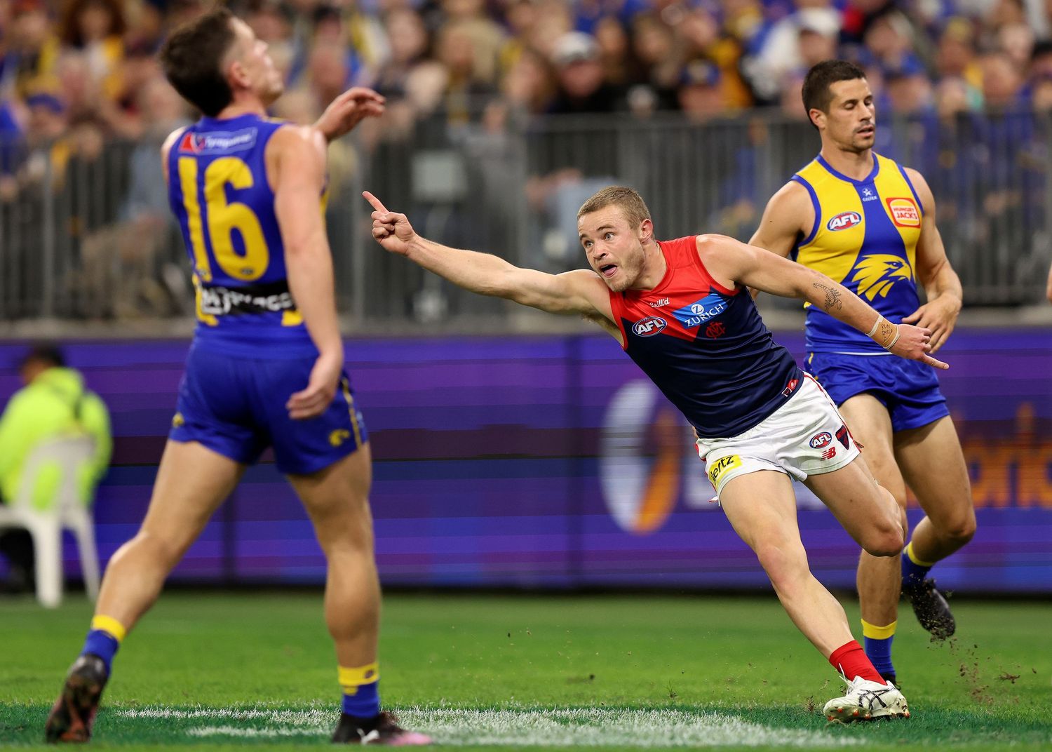 Melbourne player stretches for the ball against West Coast defenders in AFL match.