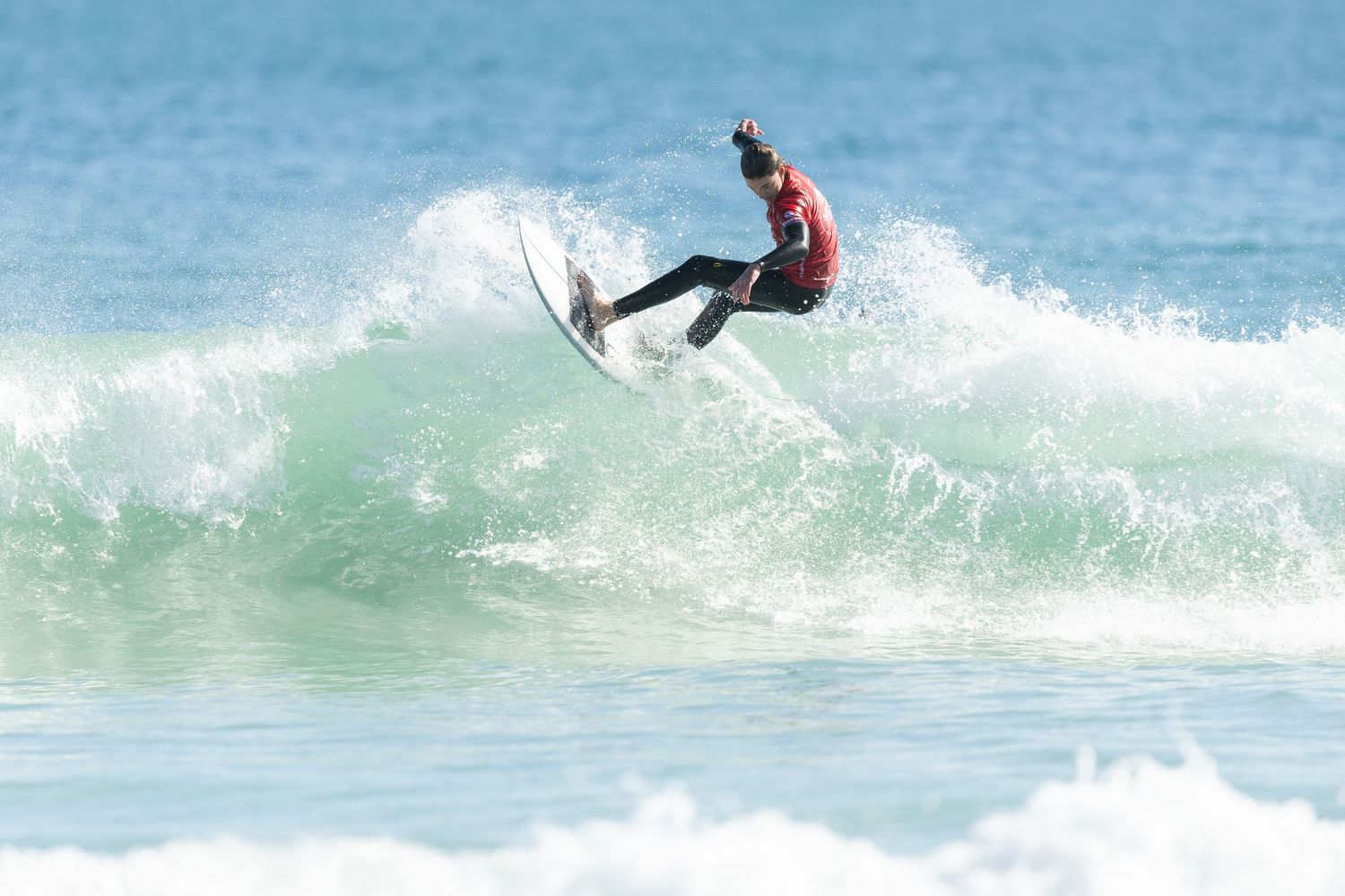 A surfer executes an aerial maneuver above a breaking wave, performing a dynamic flip over turquoise waters.