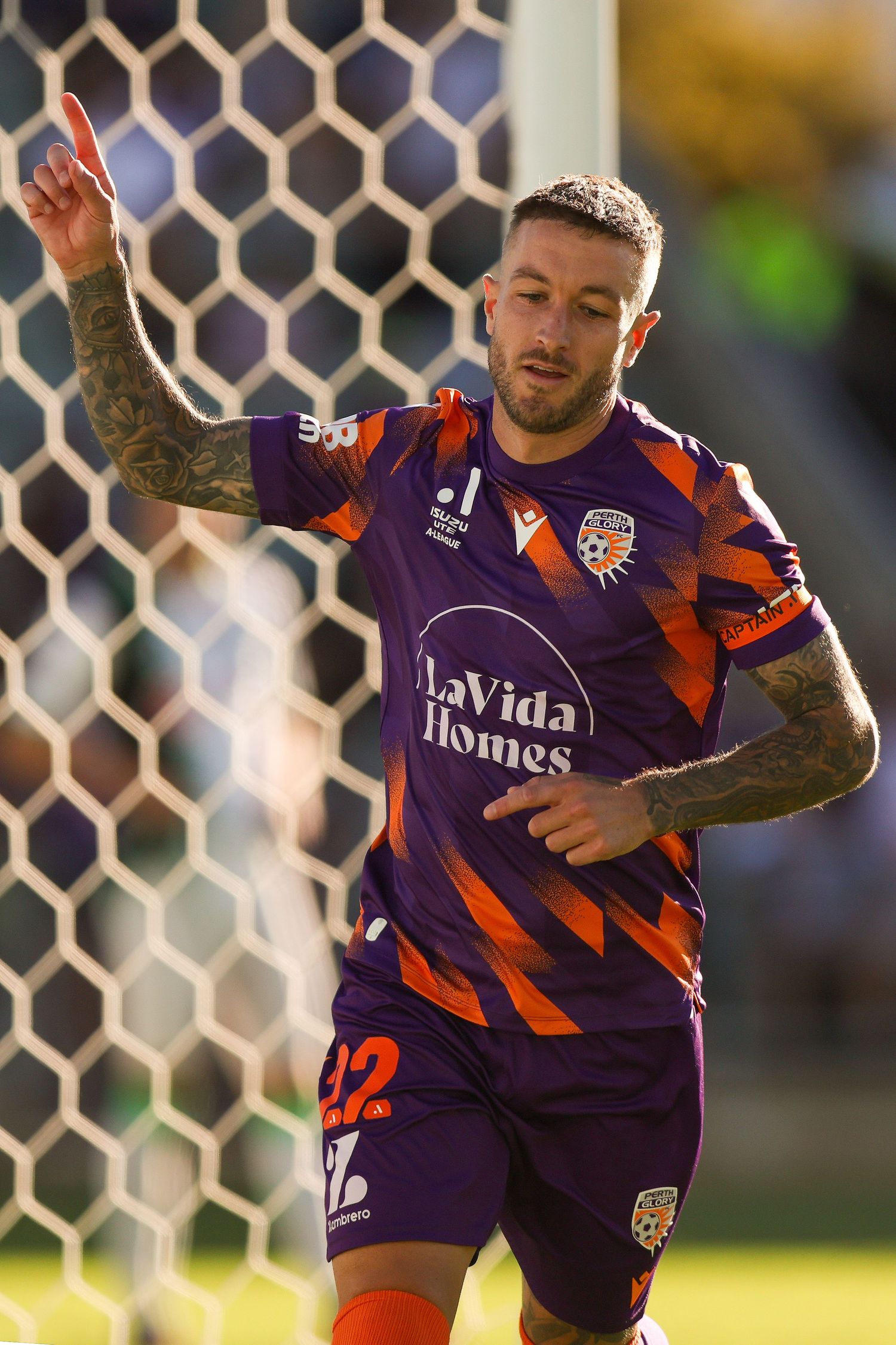 Soccer player in purple jersey celebrates near goal post.