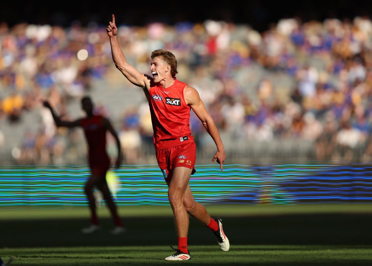 AFL player celebrates with raised arm on field during match with crowd in background.