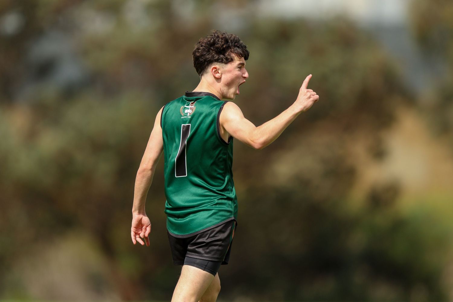 Athlete in green jersey number 7 celebrates with raised finger during outdoor sports match.