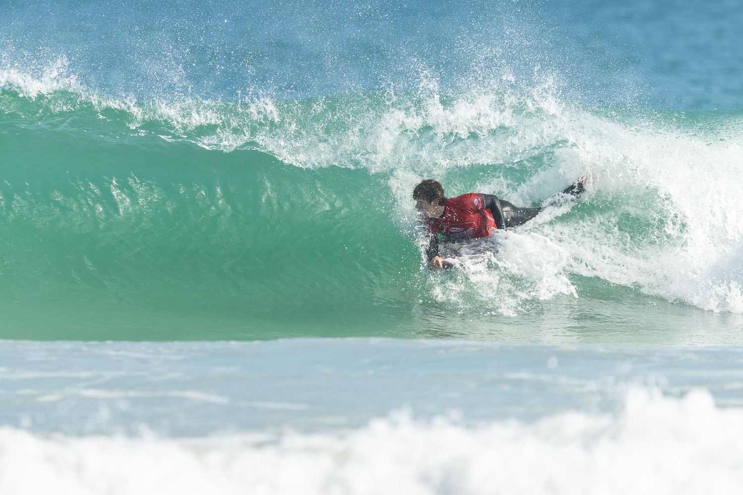 Surfboard emerging from turquoise wave during high-action surf session in bright sunny day with foaming whitewater.