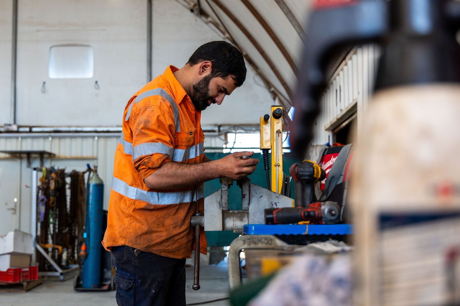 Industrial worker in orange safety vest operating machinery and equipment in manufacturing facility.