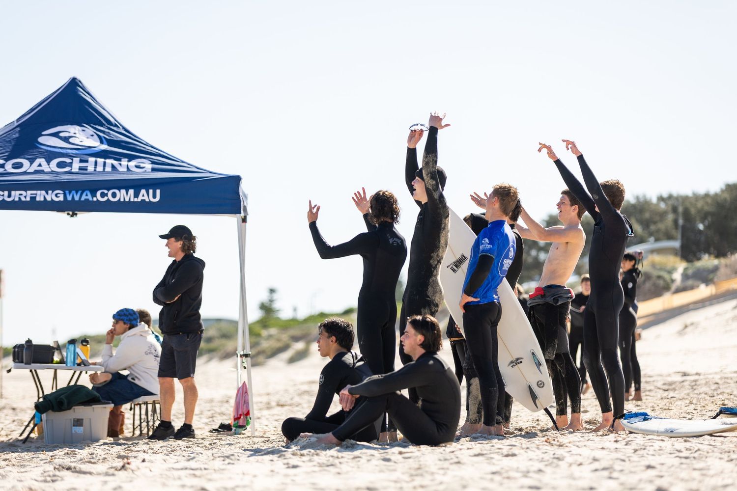 Multiple people doing yoga poses and exercises on a sunny beach during an outdoor fitness class session.