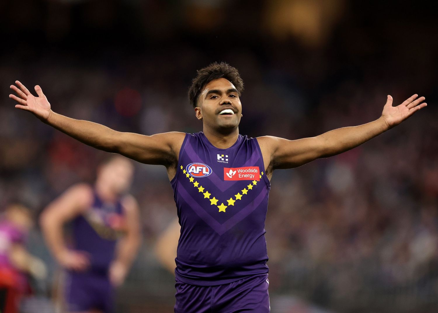 AFL player celebrates goal with arms outstretched towards the crowd during an intense match at the stadium.