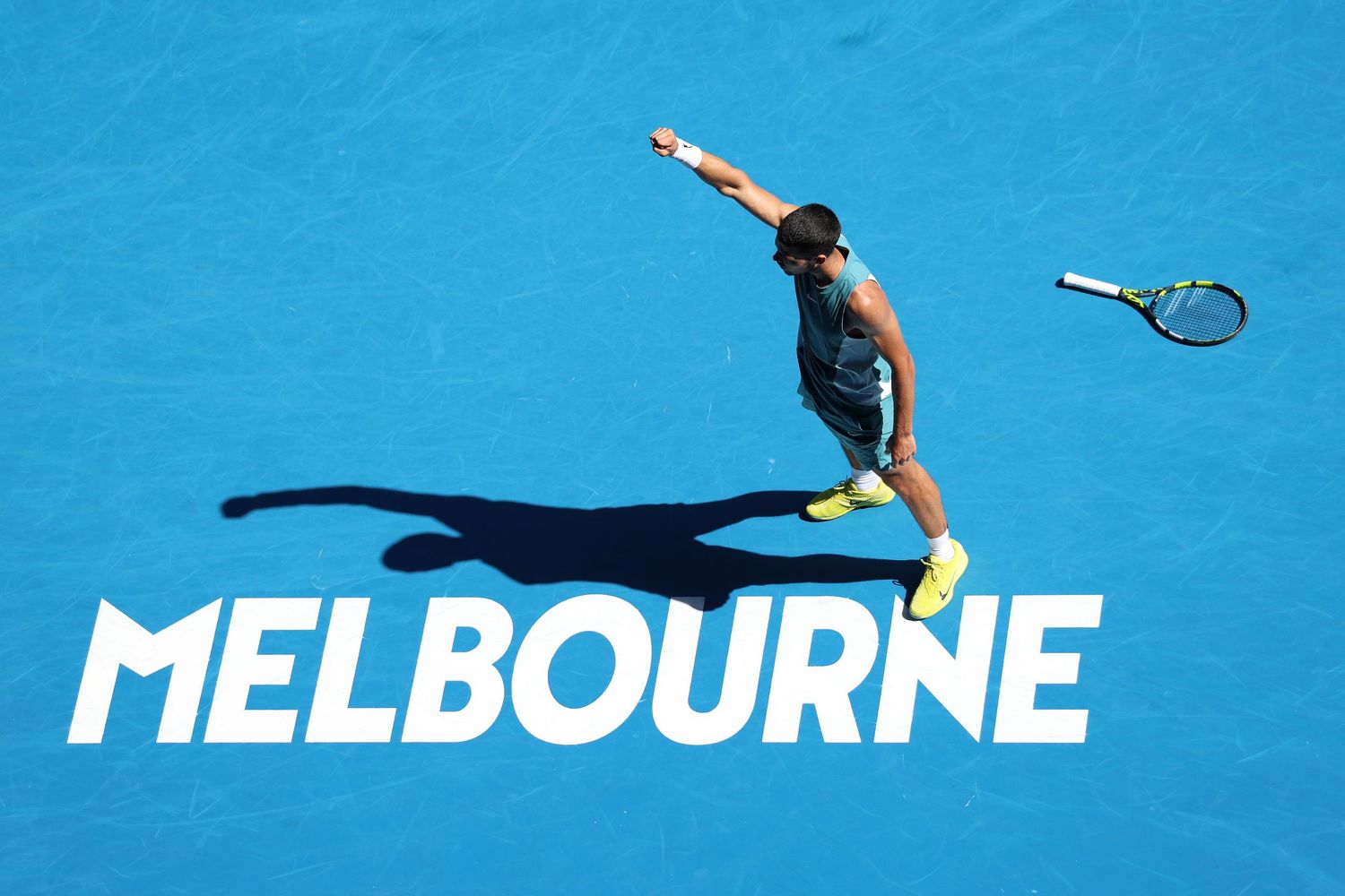 Tennis player mid-serve on blue Melbourne court with racquet throwing motion.