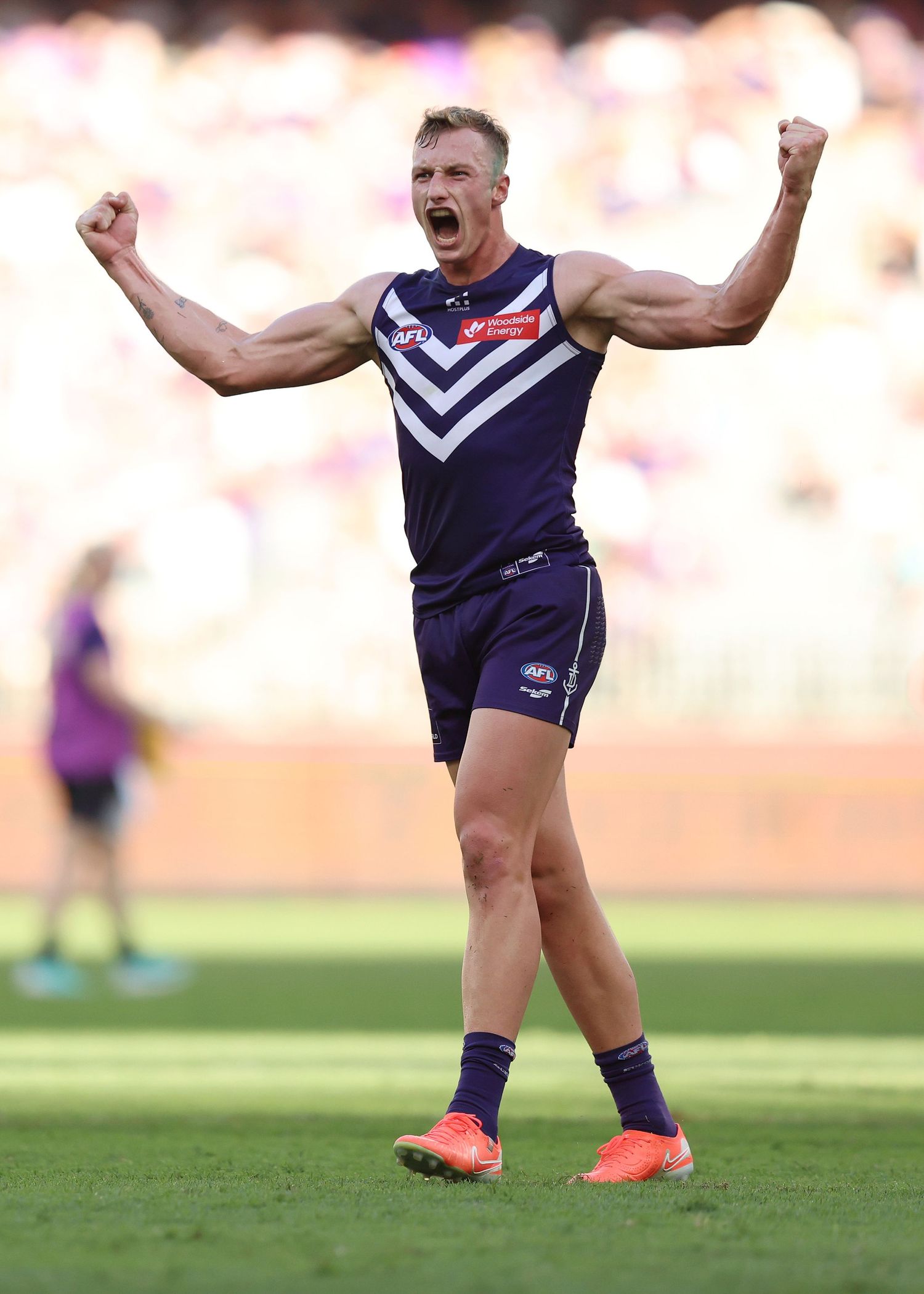 Player in Fremantle Dockers uniform celebrates victoriously on field with arms raised.