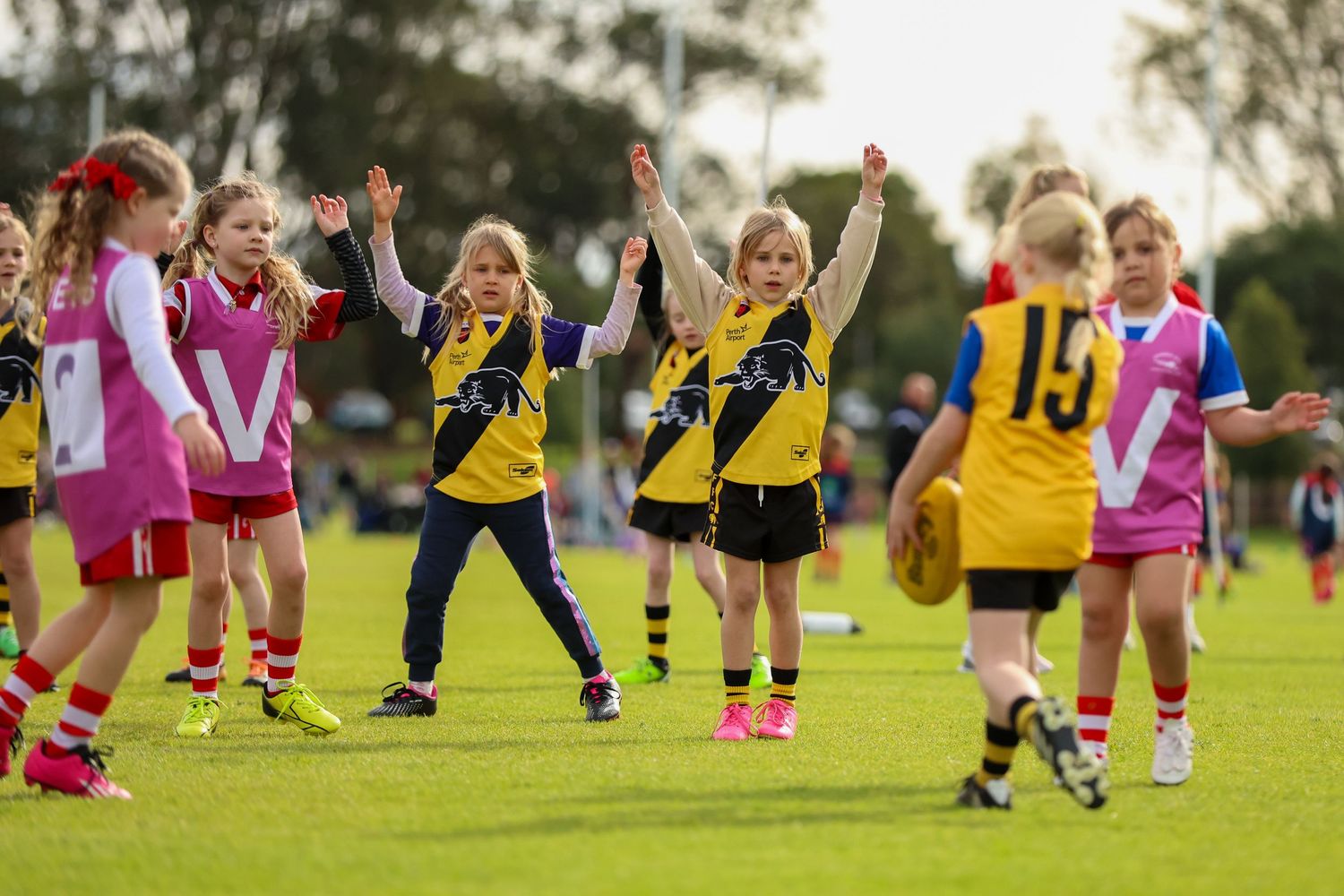 Young athletes celebrate on a sunny sports field during a youth sports match, wearing yellow and pink uniforms.