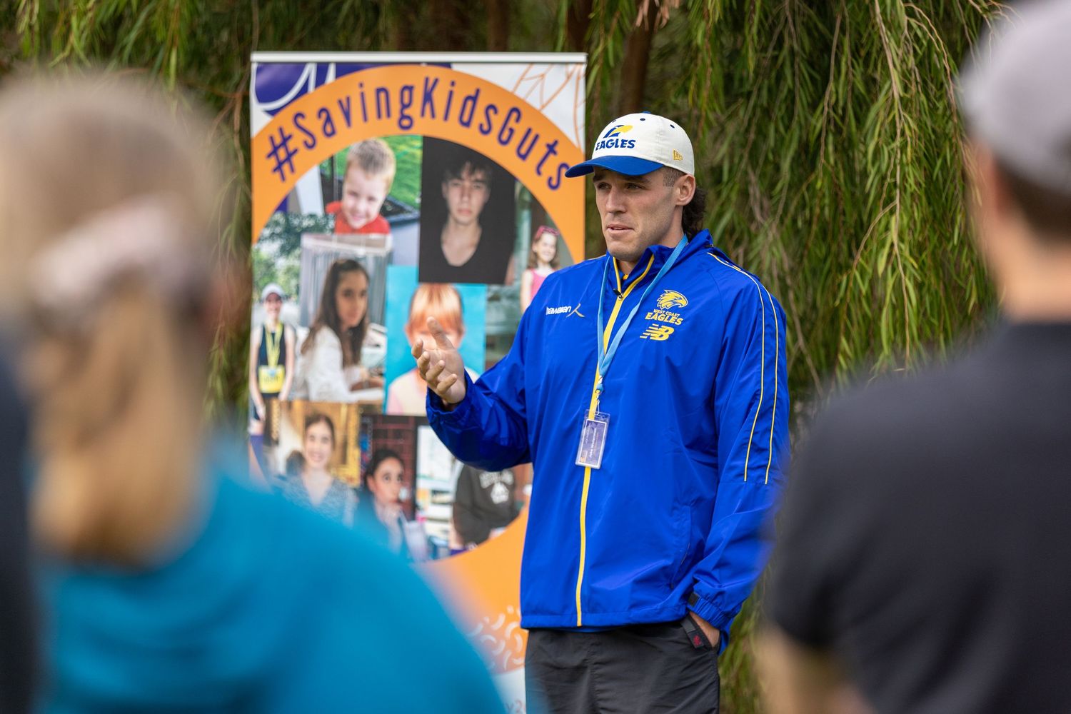 Instructor in blue jacket speaking to a group outdoors with a display board visible behind.