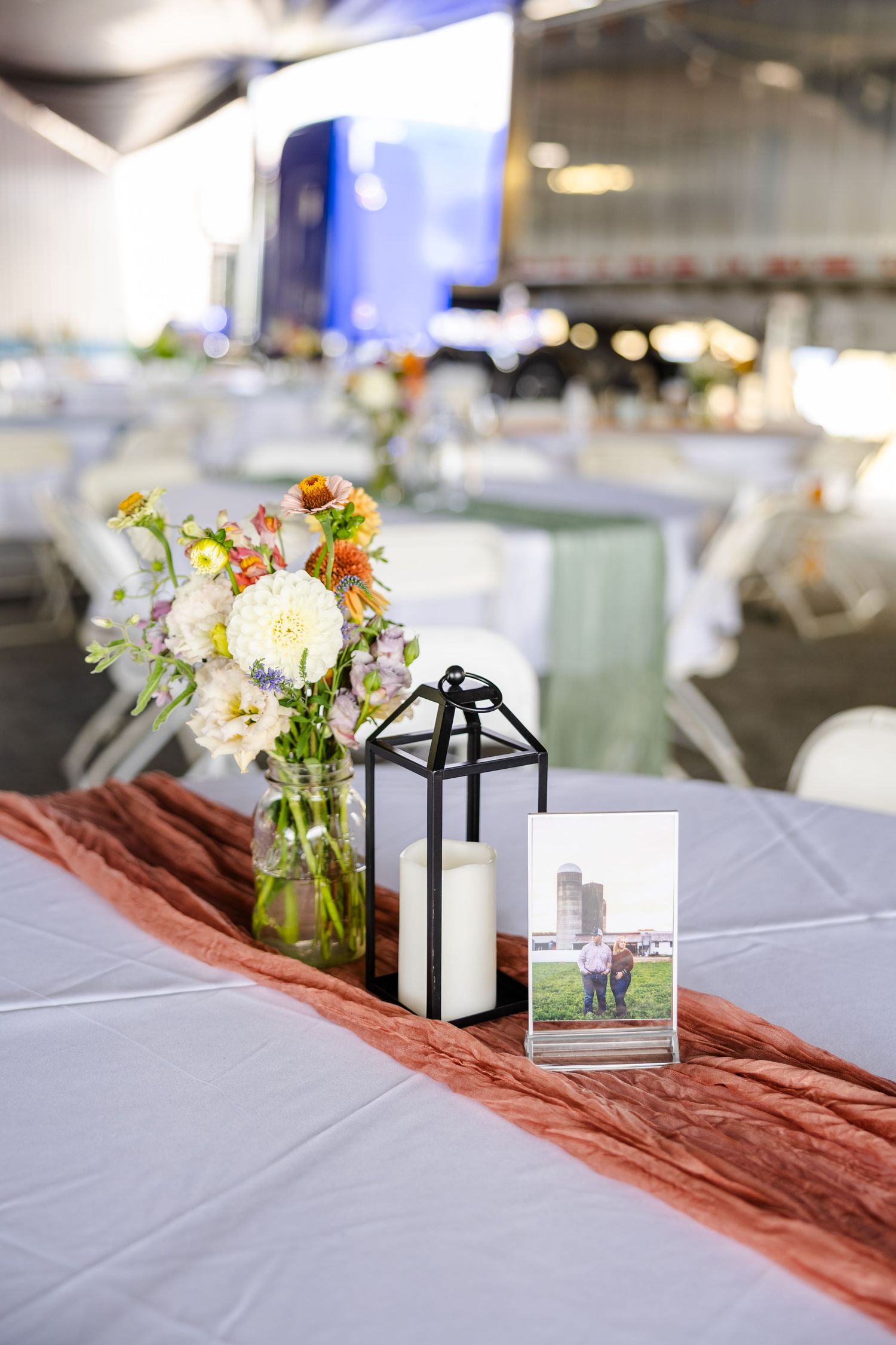 Elegant wedding reception table with floral centerpiece, lantern candle, and framed couple photo.