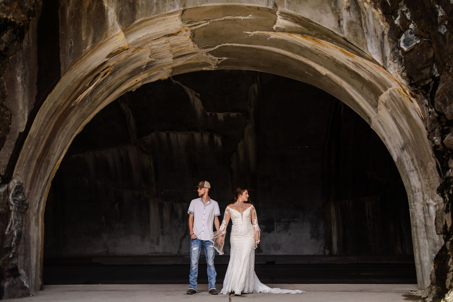 Bride and groom holding hands under a dramatic stone arch at an outdoor wedding venue.