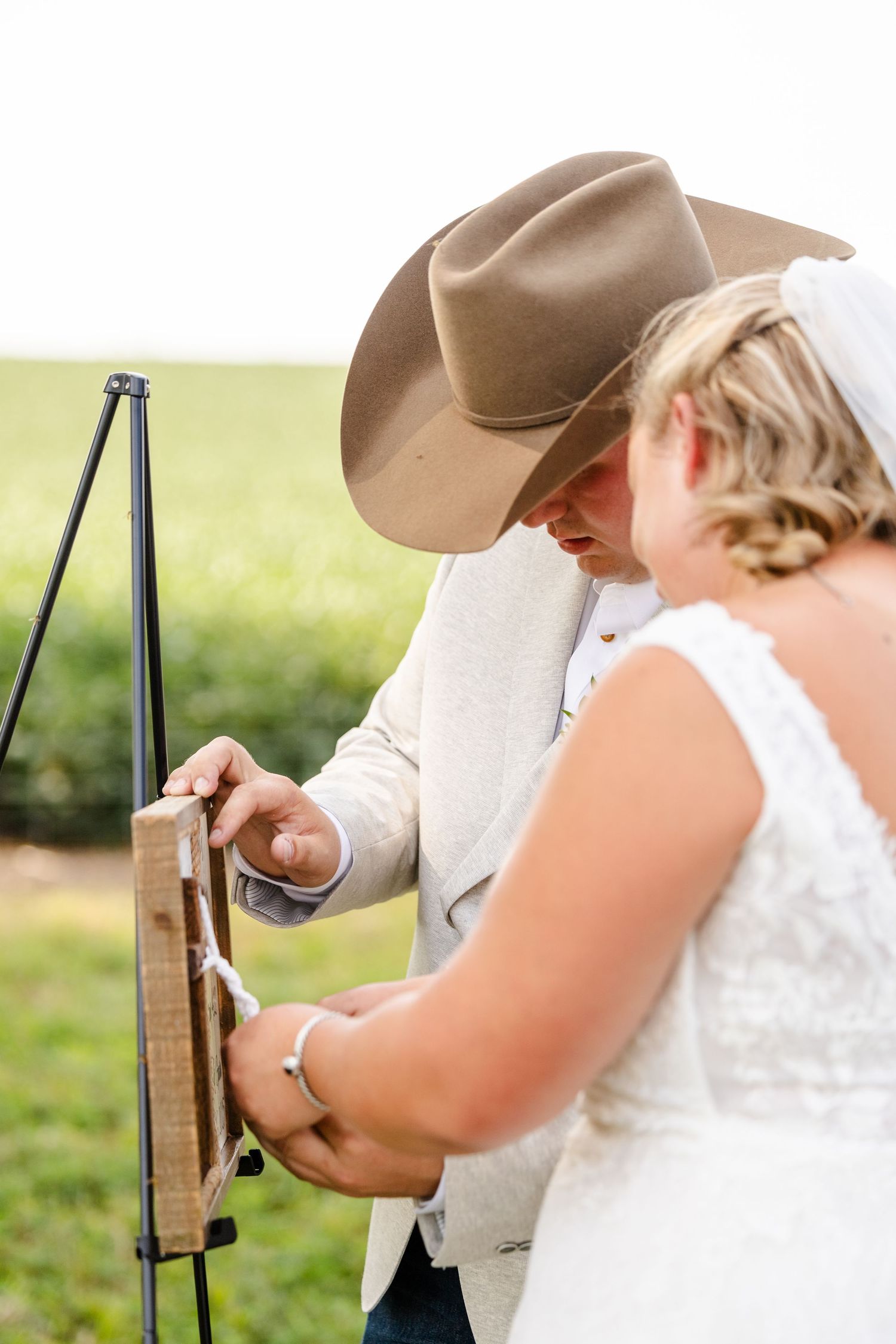 Bride and groom in cowboy hat seal a wooden unity box during their outdoor rustic wedding ceremony.