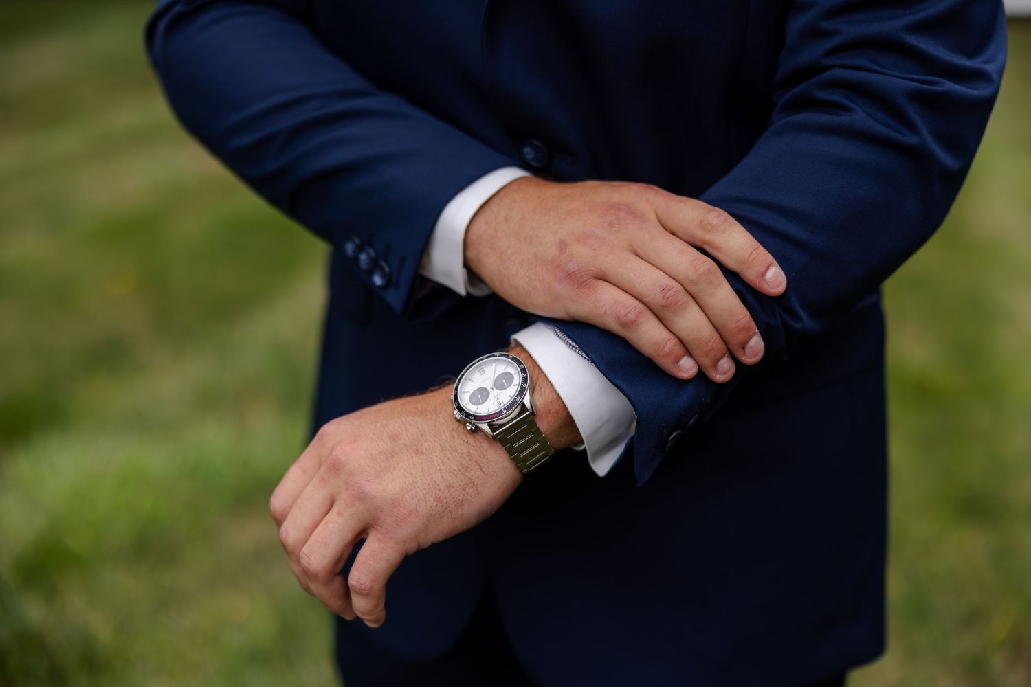 Close-up of groom in navy suit adjusting his cufflinks, wearing a classic silver wristwatch.