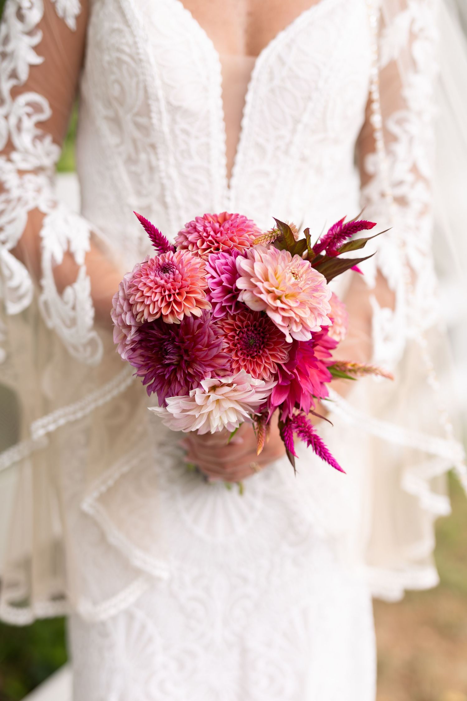Bride holds a vibrant pink and magenta dahlia bridal bouquet against her white lace wedding gown.
