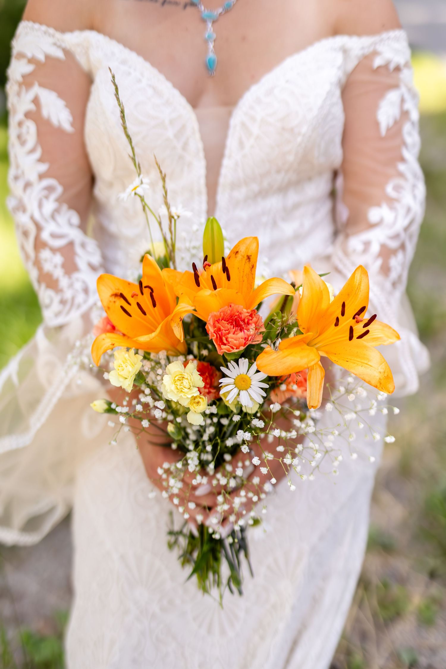 Close-up of bridal bouquet featuring orange lilies, daisies, and baby's breath held by bride in lace gown.