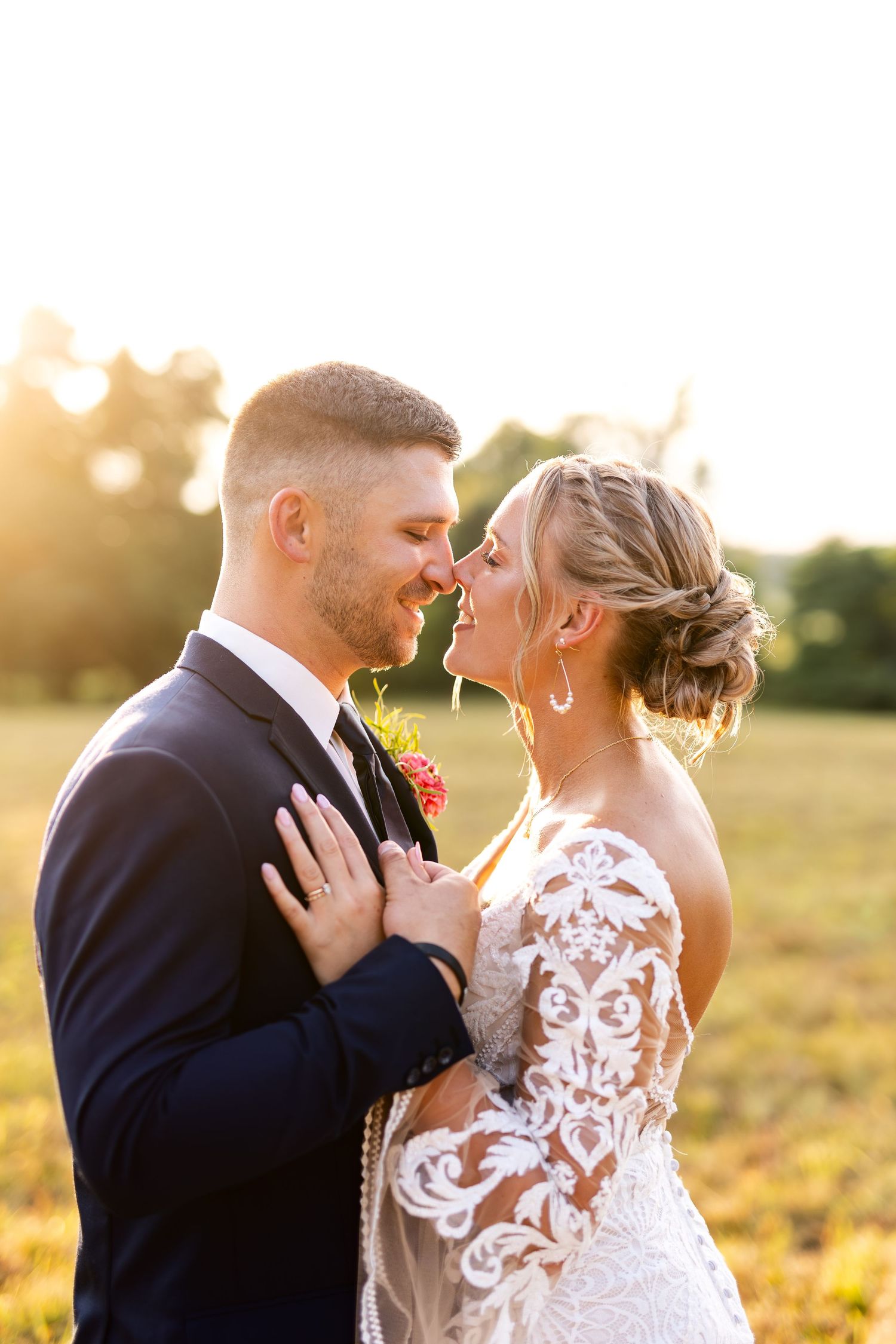 Bride and groom share a romantic golden hour moment in a field, nearly kissing in warm sunset light.