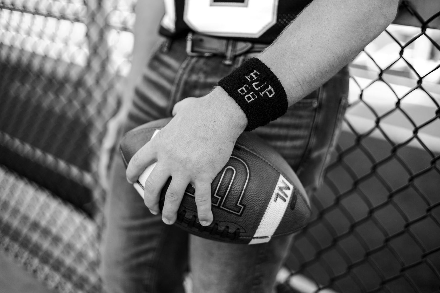 Football player holding a Wilson football with a wristband play sheet, black and white sports photography.