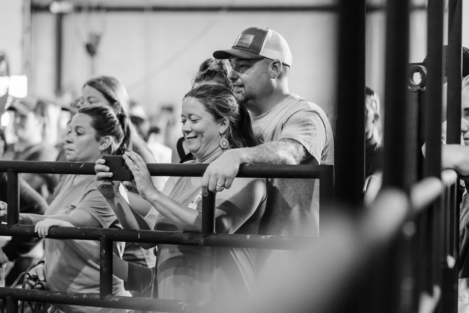 A man and woman laugh together while leaning on a fence rail at a livestock event.