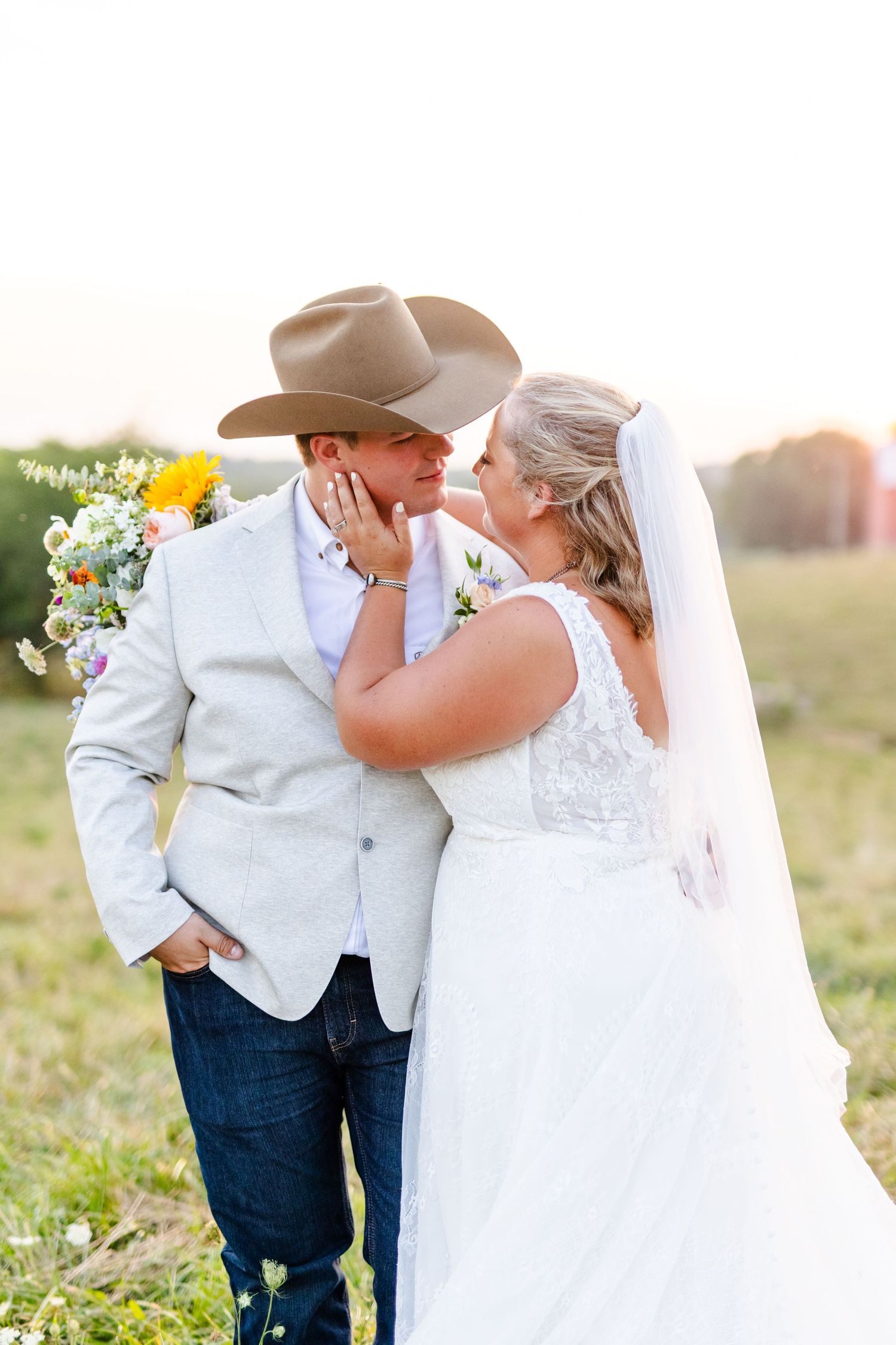 Bride tenderly holds groom's face as they share a romantic moment in a sunlit farm field.