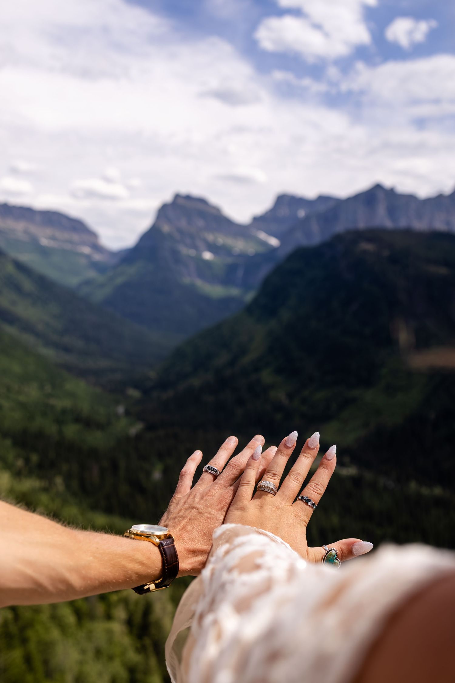 Couple displays wedding rings with hands outstretched over a stunning mountain valley landscape.