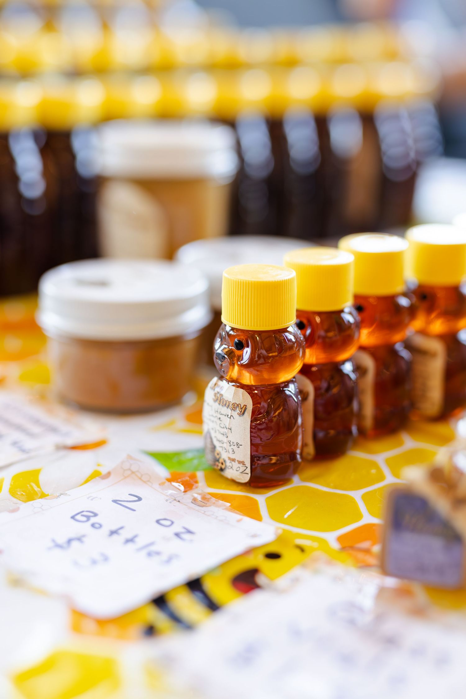 Small bear-shaped honey bottles with yellow lids displayed at a farmers market honey stand.