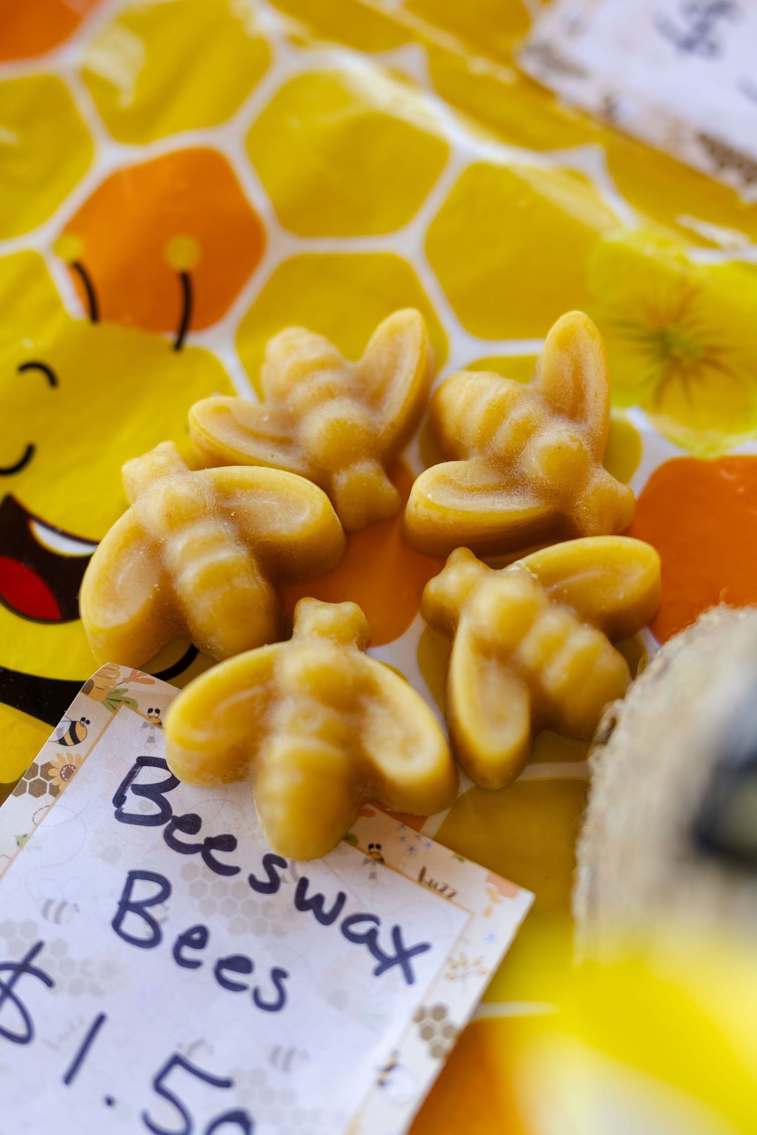 Handmade beeswax bee-shaped candles priced at $1.50 on a honeycomb patterned surface.