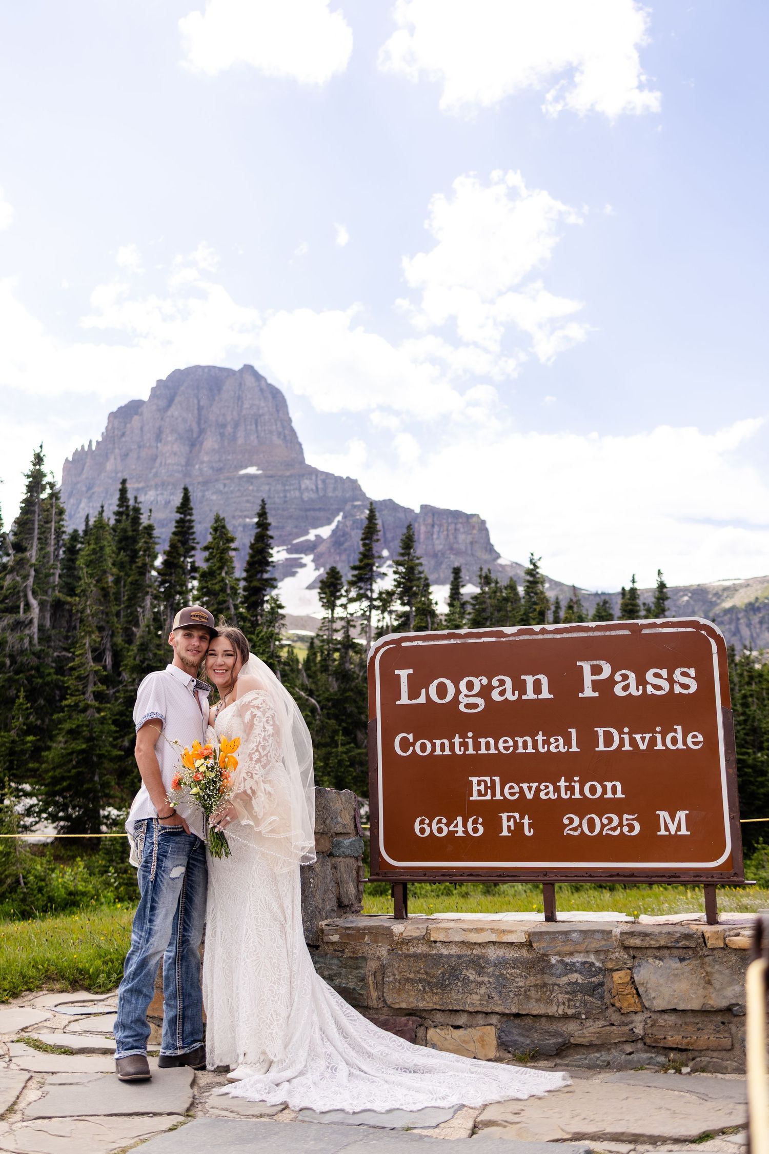 Couple embraces at Logan Pass Continental Divide sign at 6646ft elevation in Glacier National Park on wedding day.