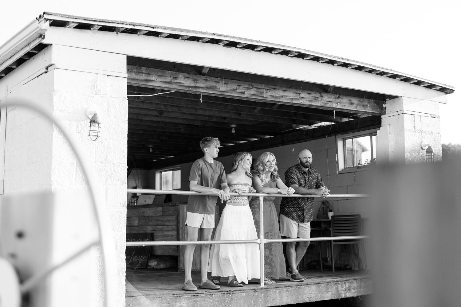 Black and white photo of wedding party standing on a rustic wooden deck overlooking a marina.