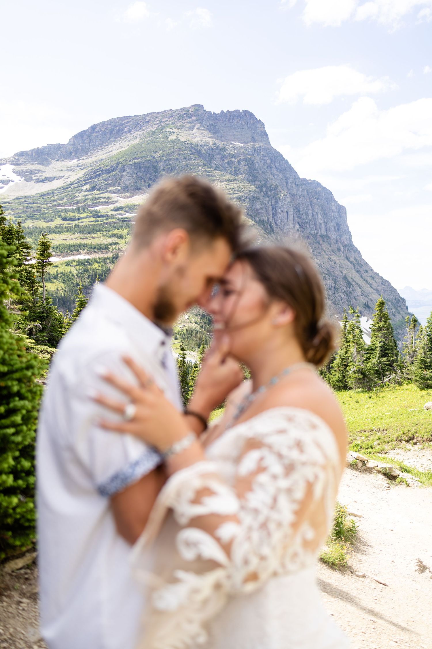Couple sharing an intimate moment in wedding attire with a stunning mountain landscape in Glacier National Park.